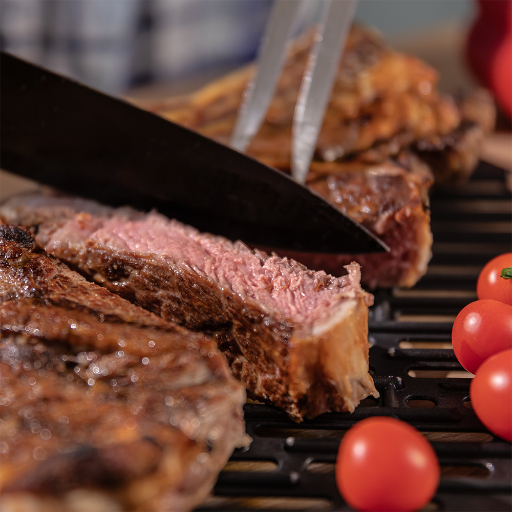 Cuchillo cortando un filete jugoso en una parrilla junto a tomates cherry.