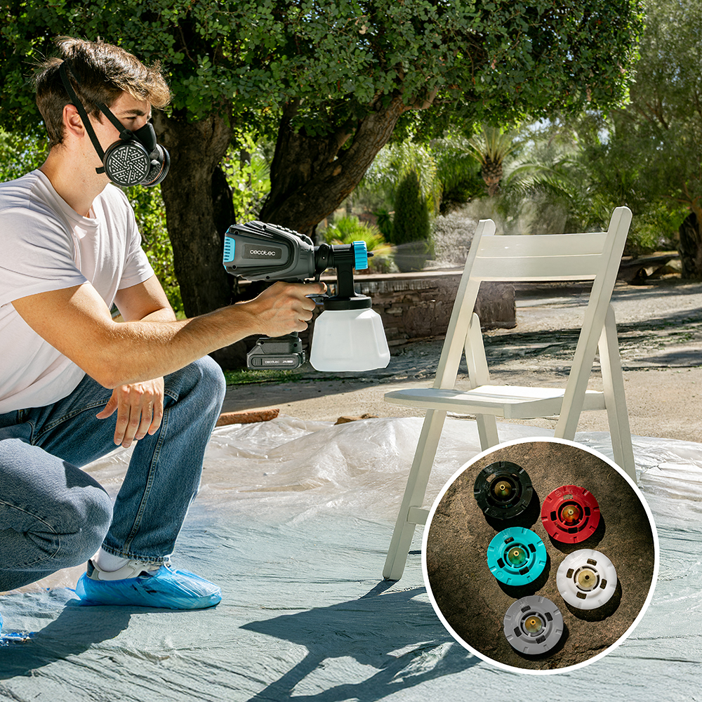 Un uomo con maschera dipinge una sedia bianca all'aperto, con ugelli intercambiabili in un riquadro.