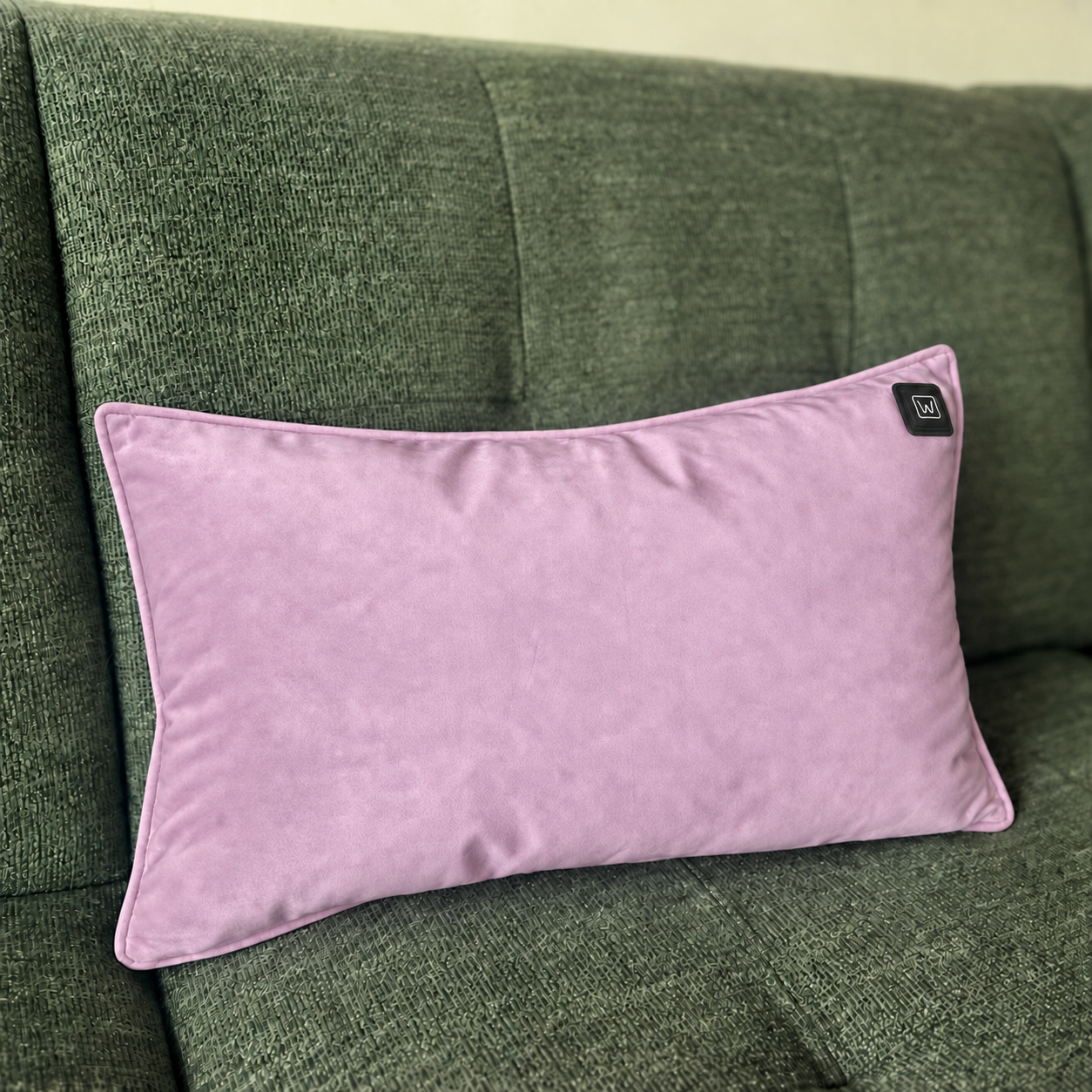 Ein rosafarbenes Kissen mit einem kleinen schwarzen Etikett liegt auf einer grünen Couch.