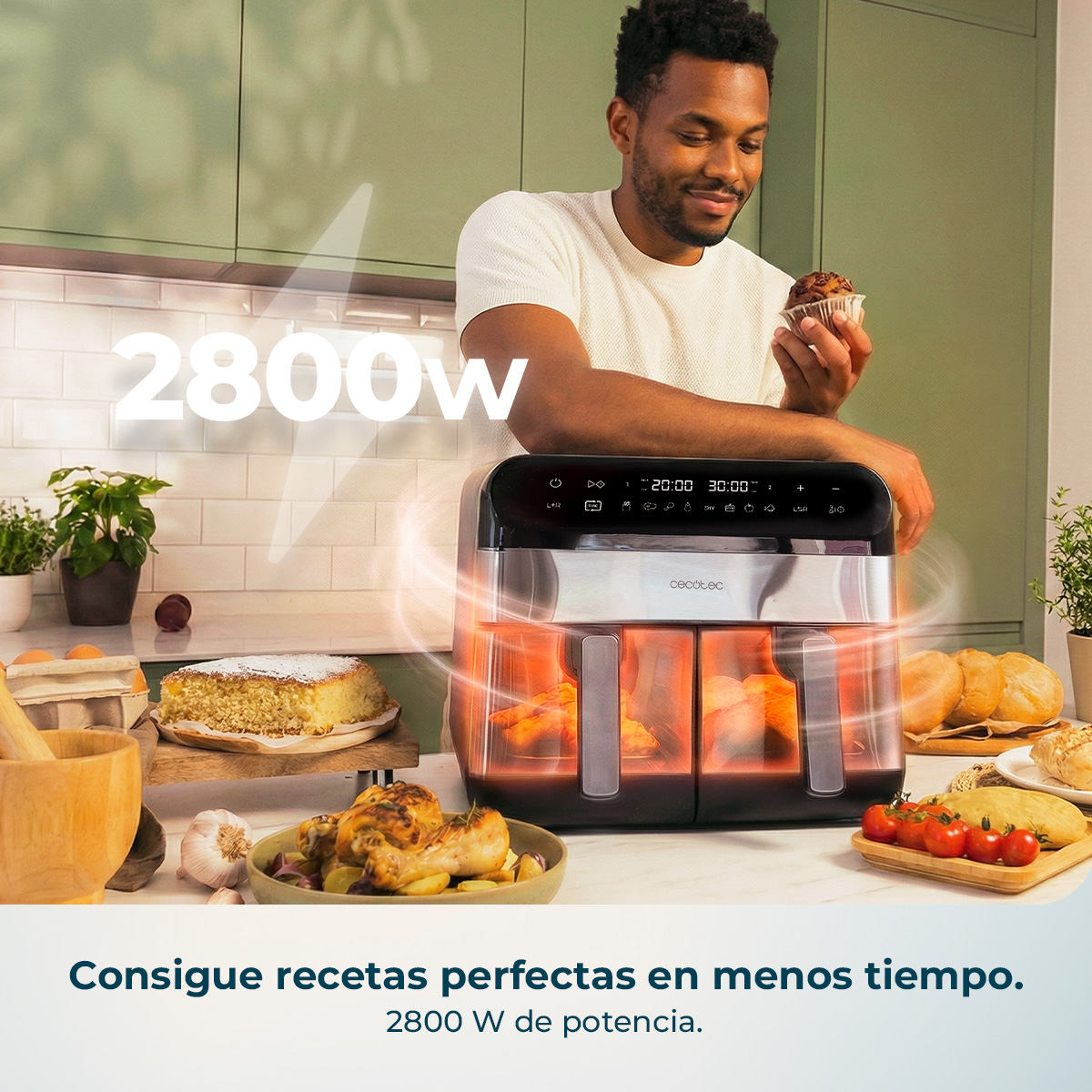Un hombre en una cocina sostiene un panecillo frente a una gran freidora de aire de doble zona con alimentos.