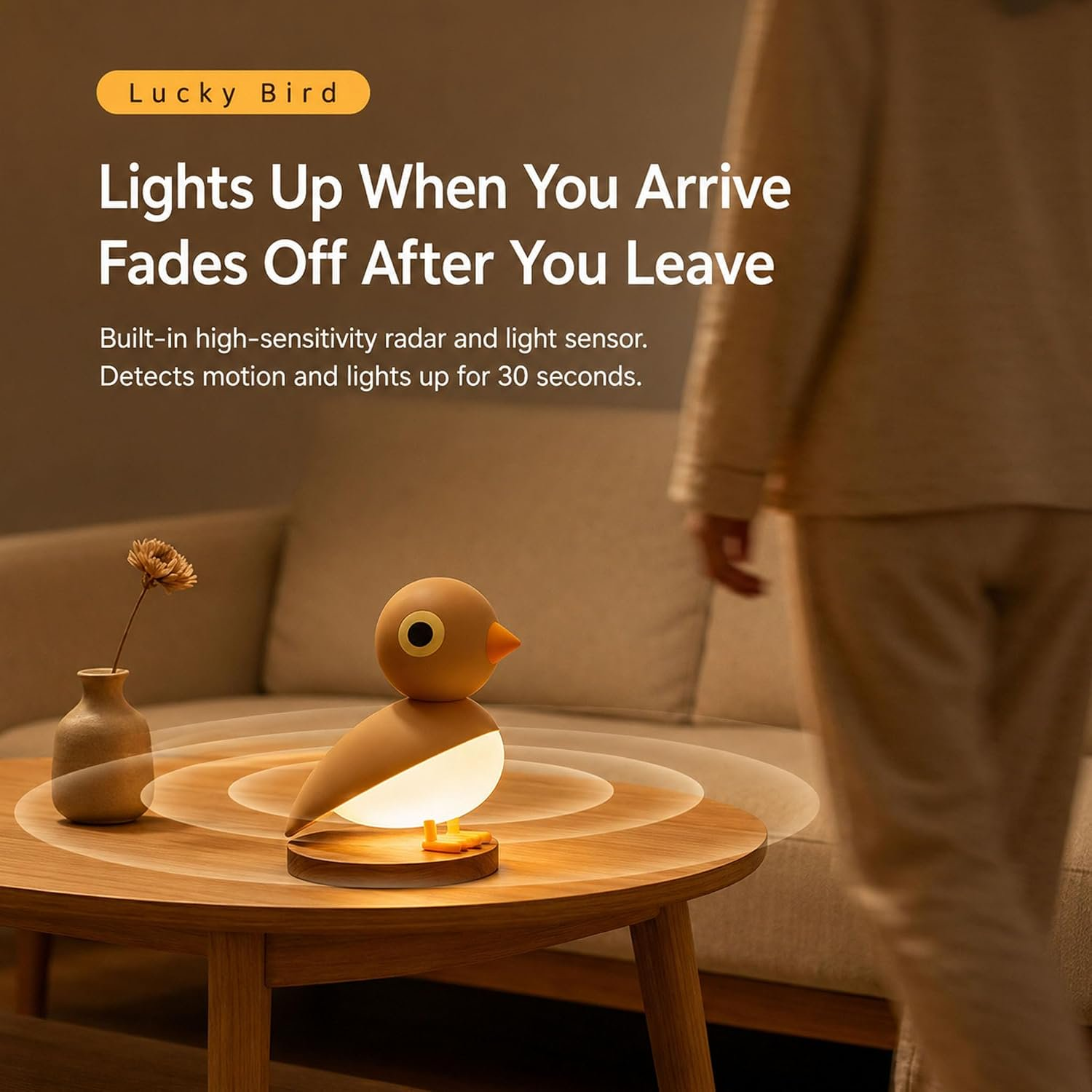 Eine kleine vogelförmige LED-Lampe leuchtet auf einem Holztisch, während eine Person im Hintergrund steht.