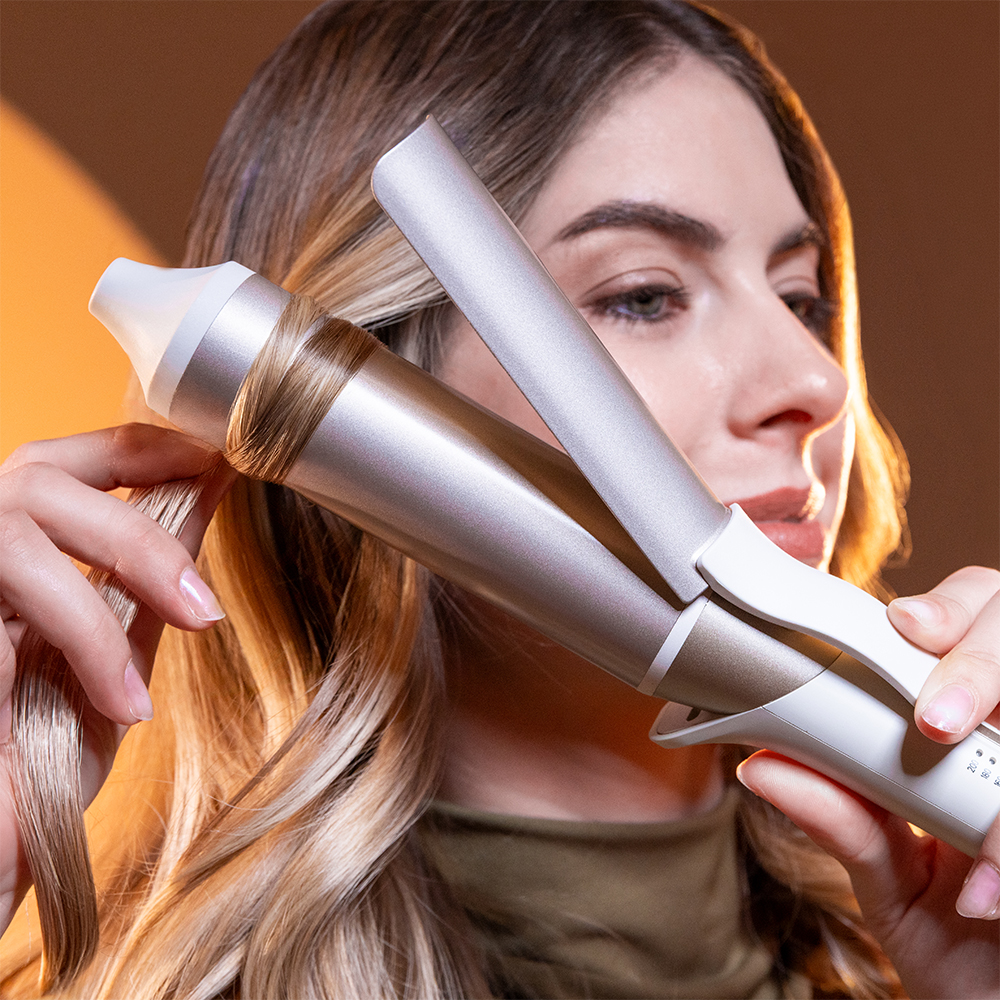 Una donna acconcia i suoi capelli biondi usando un ferro arricciacapelli automatico.