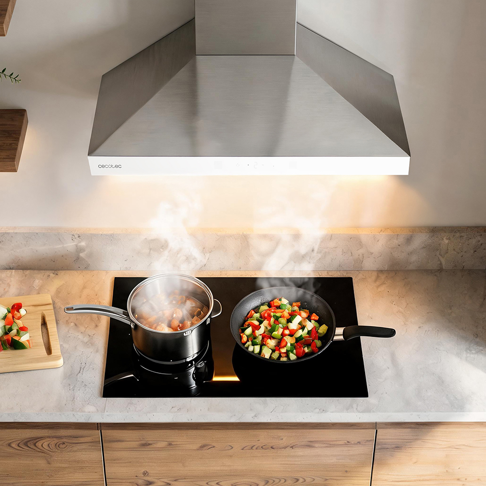 Campana extractora sobre placa con olla humeante y sartén de verduras.