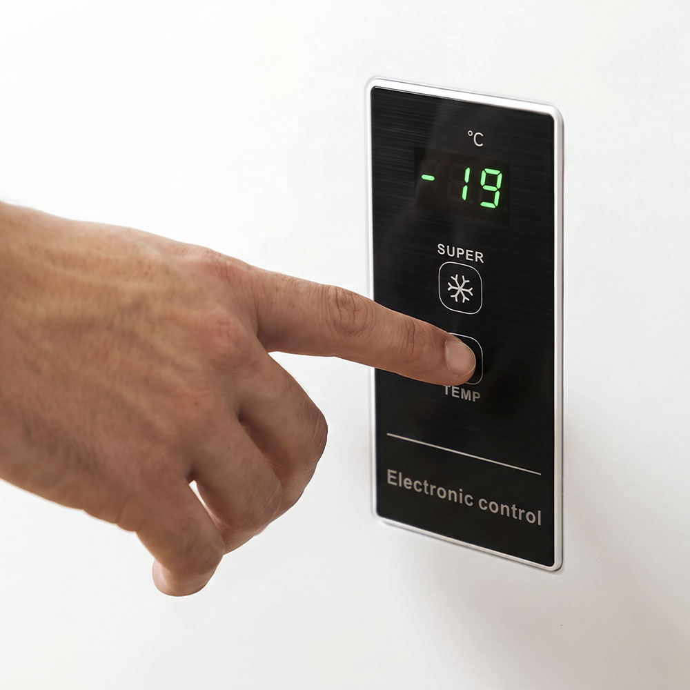 Una mano preme un pulsante sul pannello di controllo elettronico di un frigorifero che mostra meno diciannove gradi.