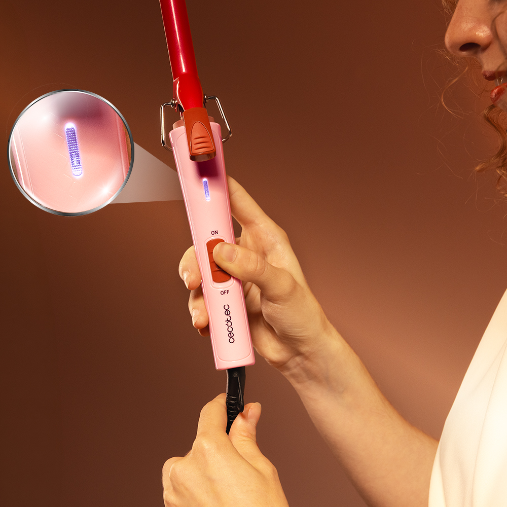 Una mano tiene un ferro arricciacapelli rosa con display illuminato, con un dettaglio ingrandito in un cerchio.