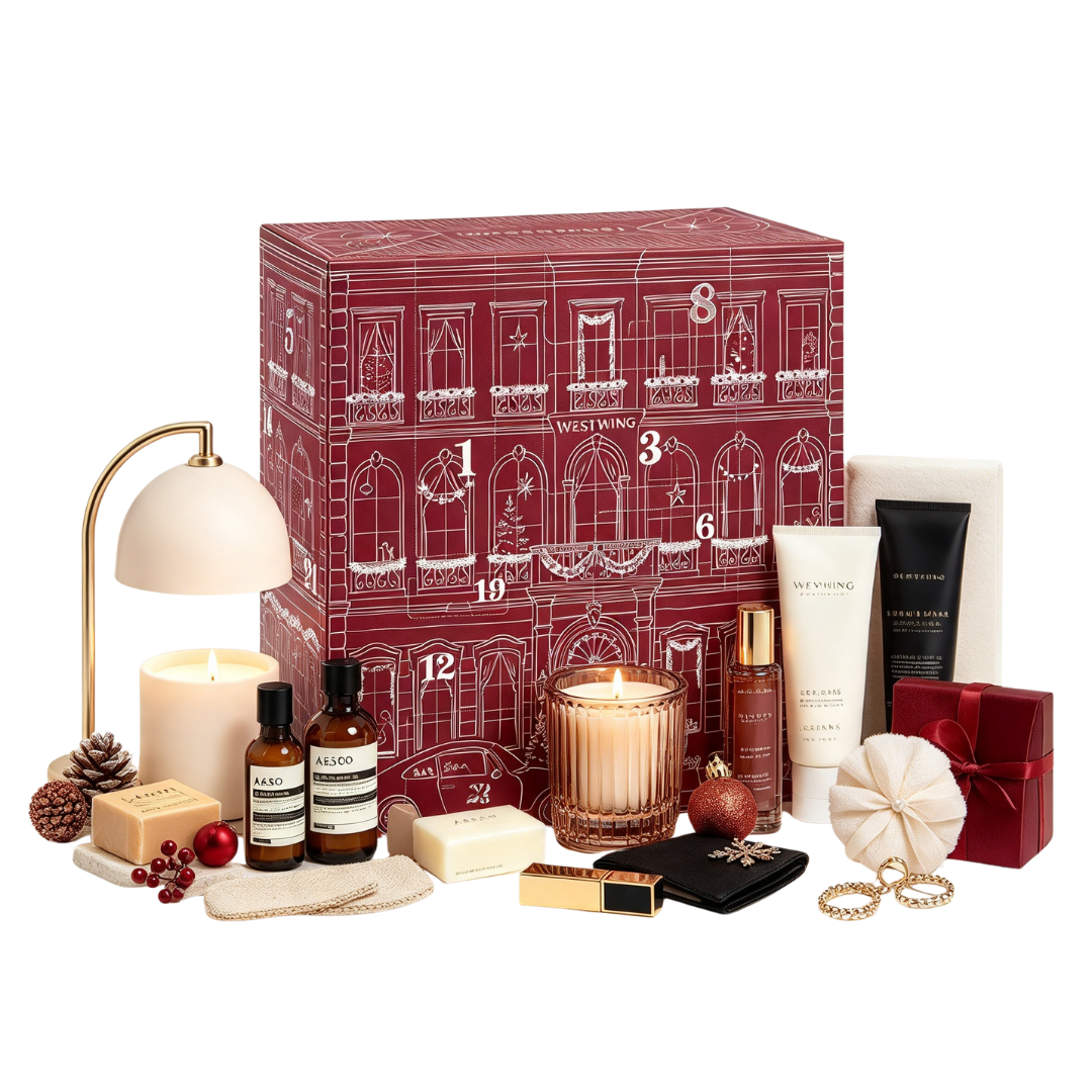 Eine große rote Adventskalenderbox, umgeben von Kosmetika, Kerzen, einer Lampe und kleiner Weihnachtsdeko.
