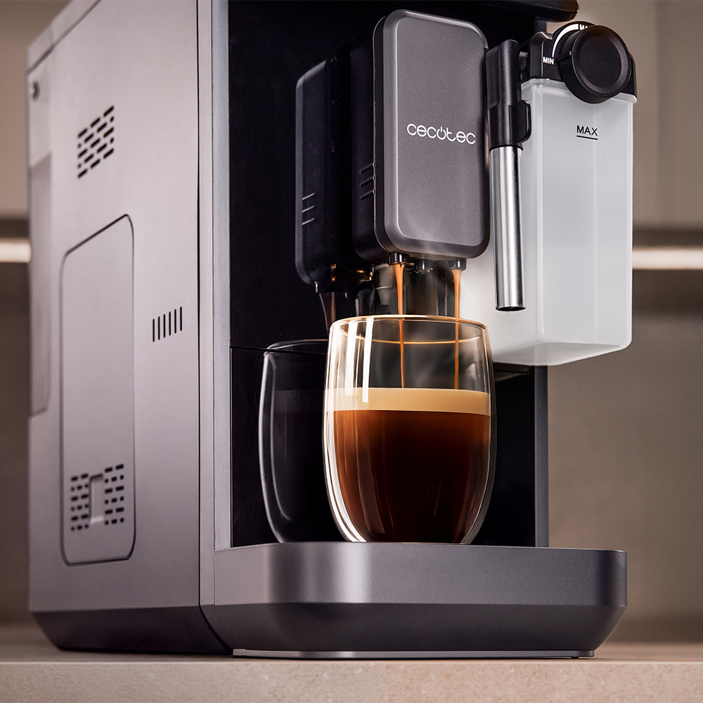 Eine graue Kaffeemaschine brüht frischen Espresso in ein doppeltwandiges Glas auf einer Theke.