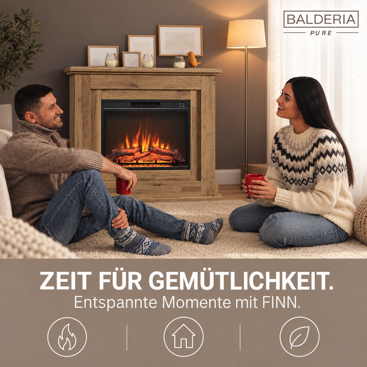Ein Paar sitzt auf dem Teppich vor einem elektrischen Kamin und hält rote Tassen in der Hand.