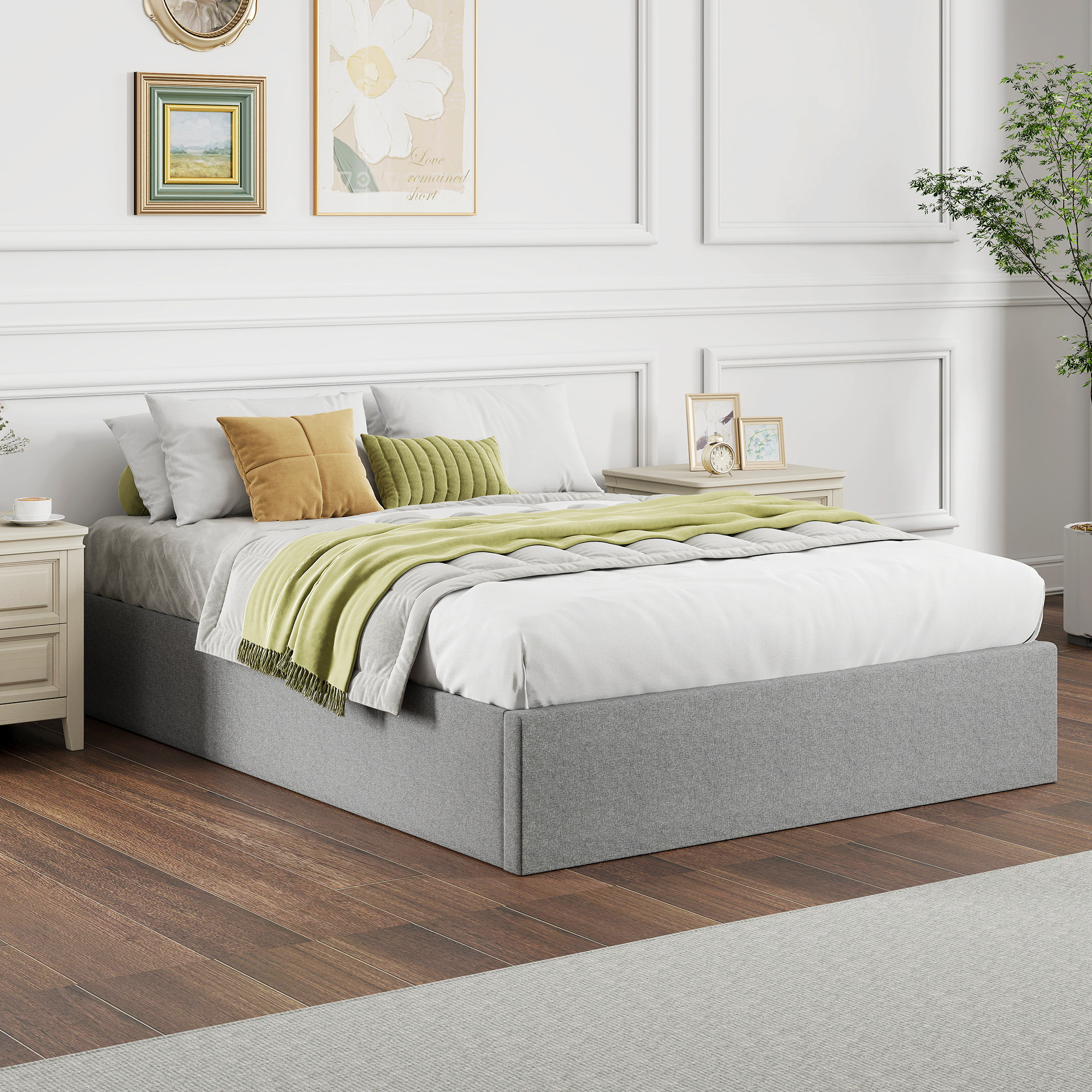 Una cama blanca con base gris, cojines amarillos y verdes, en un dormitorio luminoso con suelo de madera.