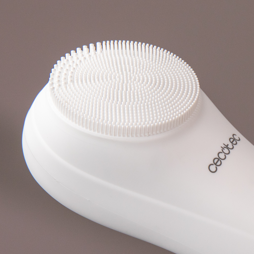 Un cepillo de limpieza facial blanco con cerdas de silicona finas sobre fondo marrón.
