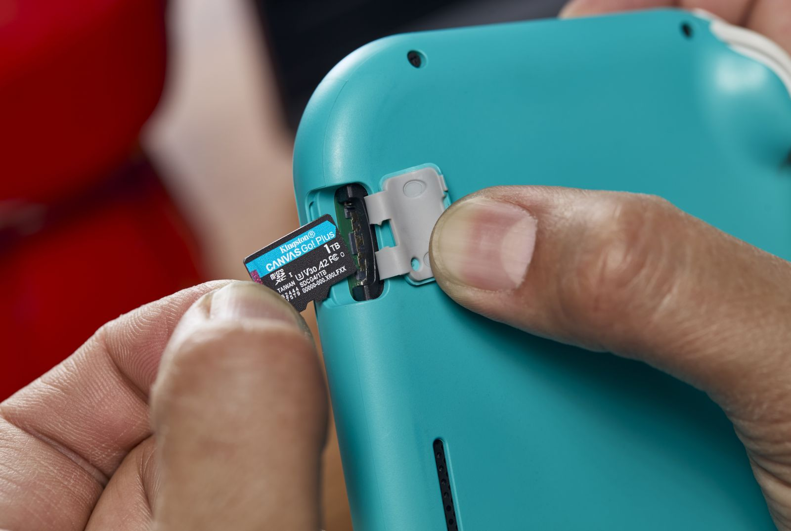 Une main insère une carte micro SD dans la fente d'une console bleu sarcelle.