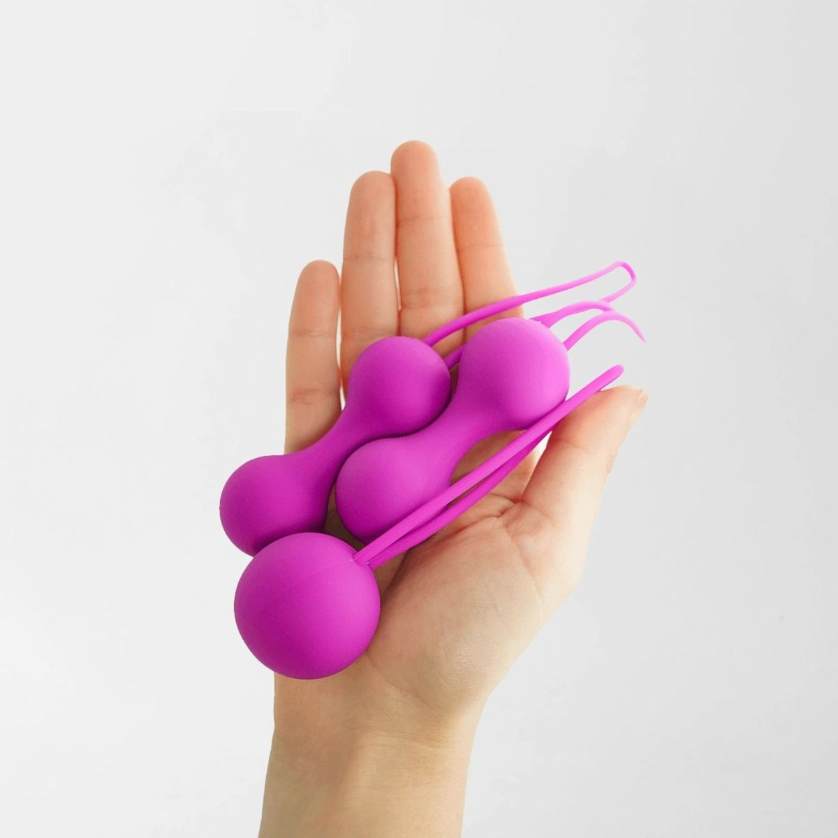 Eine offene Hand hält zwei hellrosa Silikon-Kegel-Übungsgeräte vor einem schlichten weißen Hintergrund.
