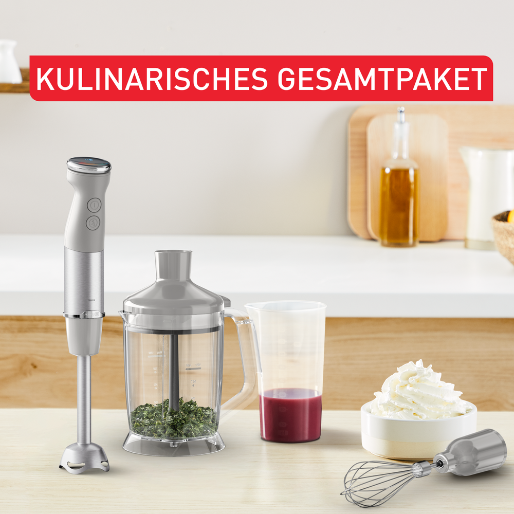 Ein silberner Stabmixer auf einer Küchenzeile mit Kräuterzerkleinerer, Messbecher und Schlagsahne.