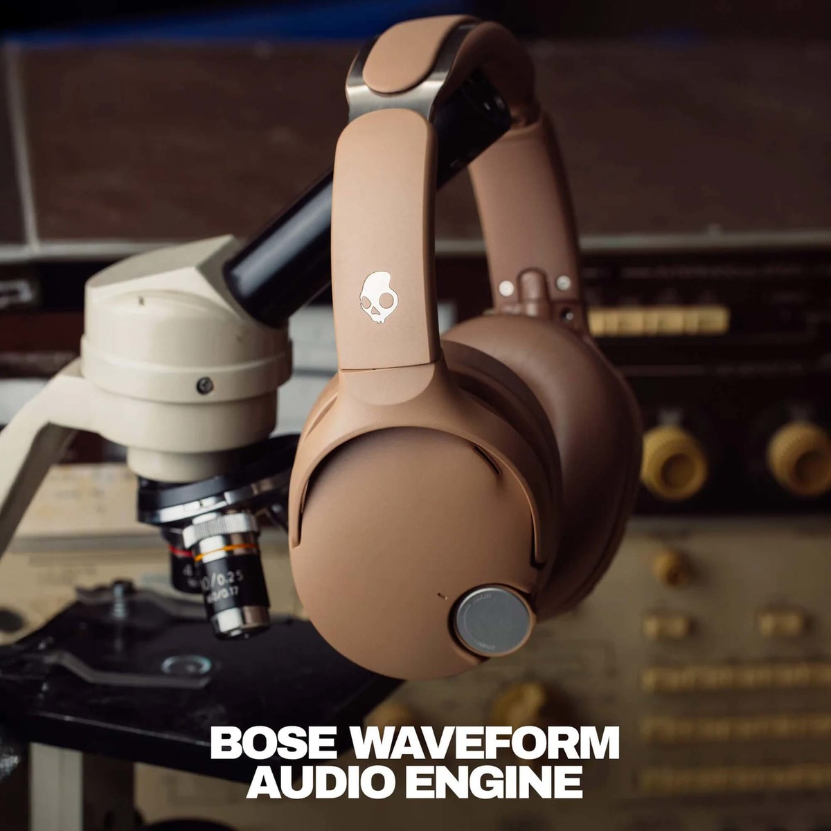 Auriculares beiges cuelgan de un microscopio en un laboratorio. El texto dice Bose Waveform Audio Engine.