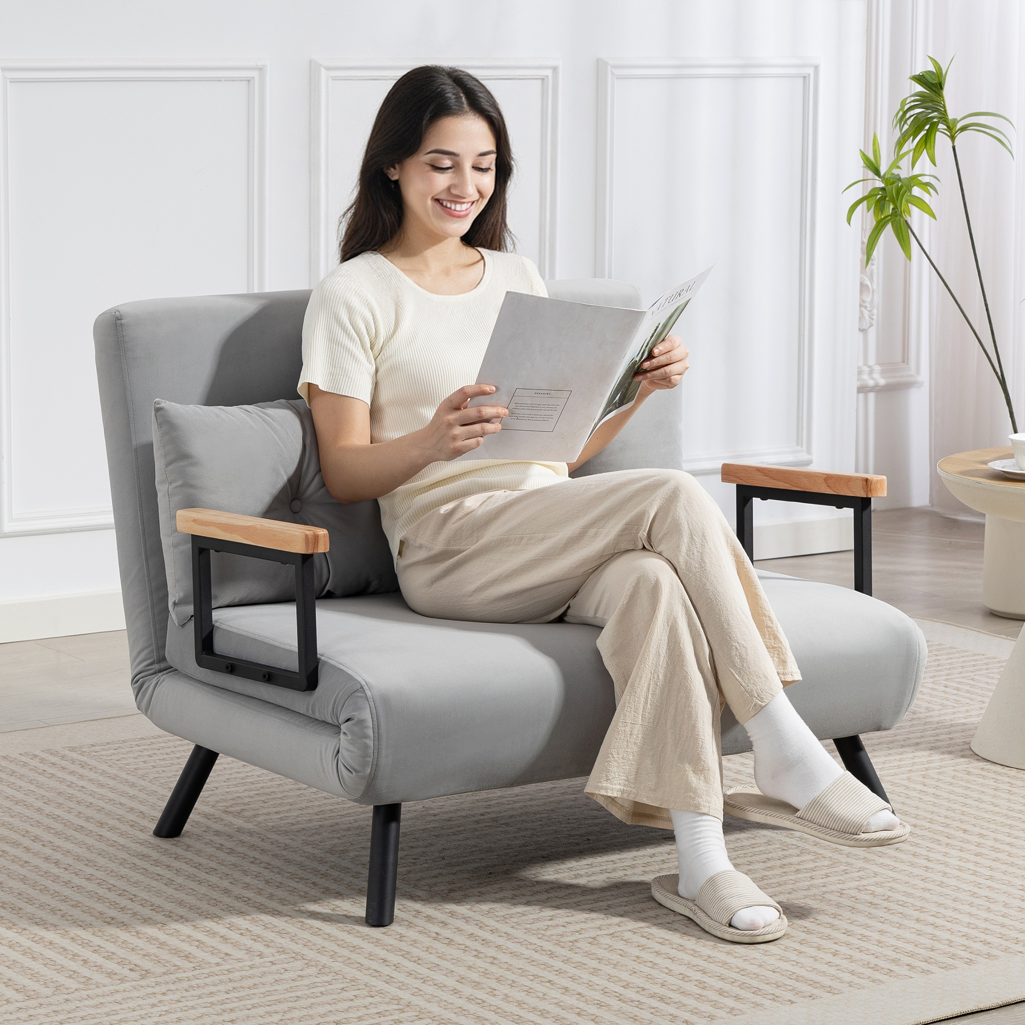 Una mujer sonriente lee una revista mientras está sentada en un sillón gris.