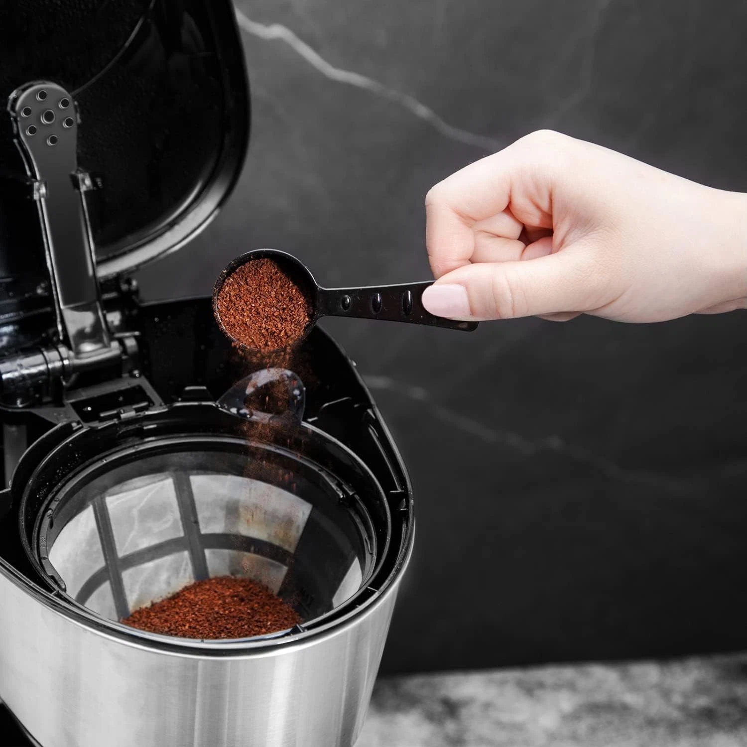 Una mano versa il caffè macinato da un cucchiaio nel filtro di una caffettiera.