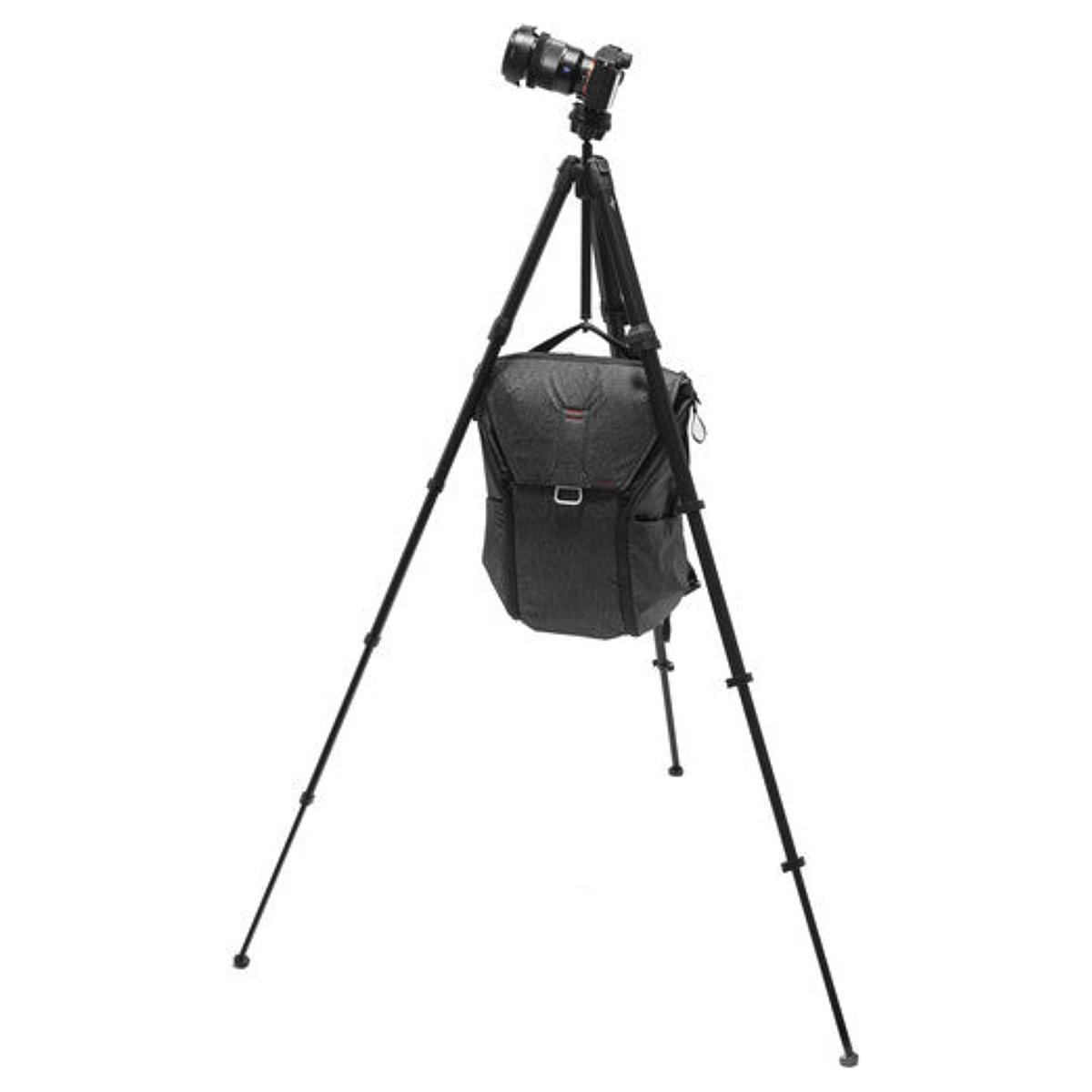 A black camera on a tripod with a dark camera bag hanging from it.