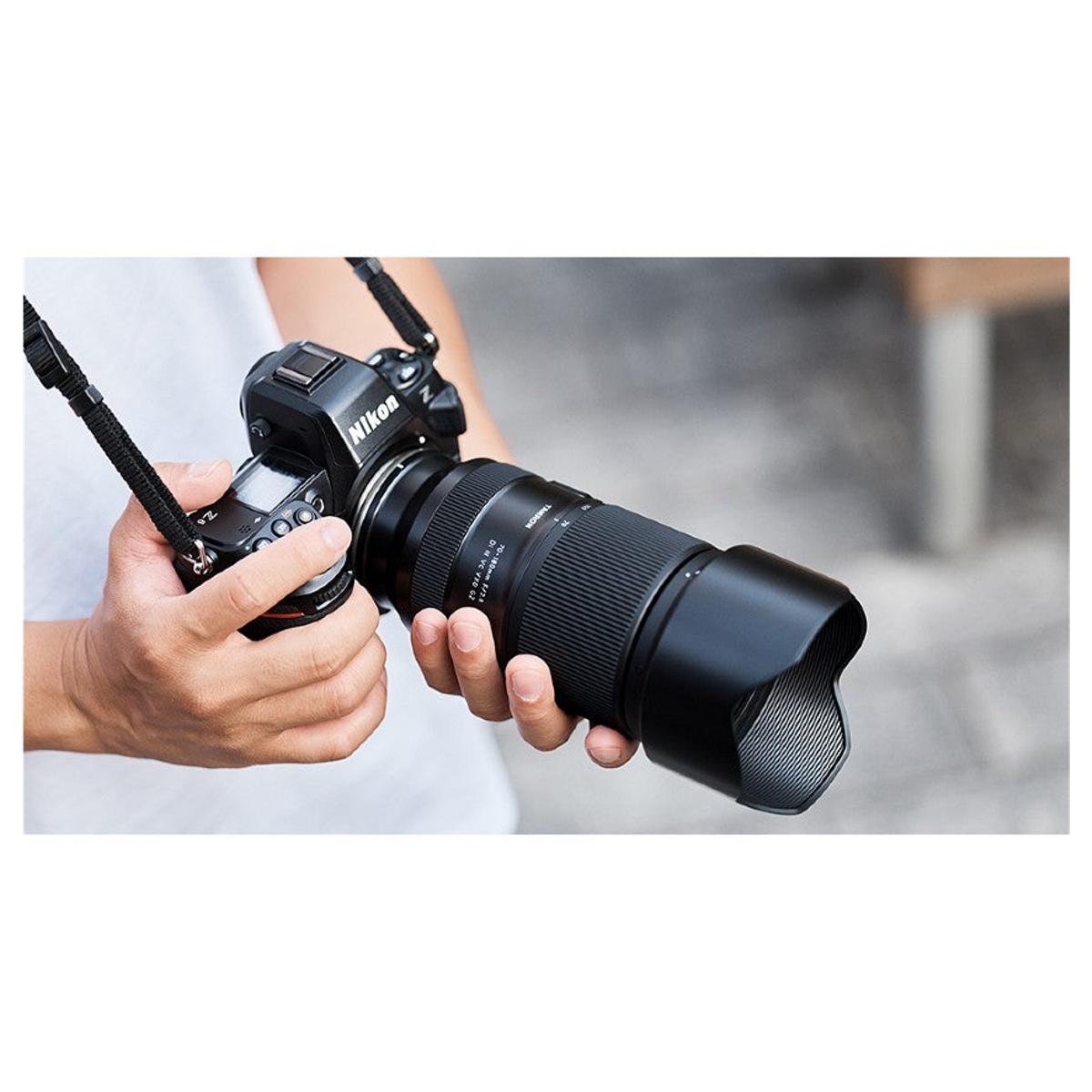 Person hält eine schwarze Nikon-Kamera mit langem Objektiv und Tragegurt in den Händen.