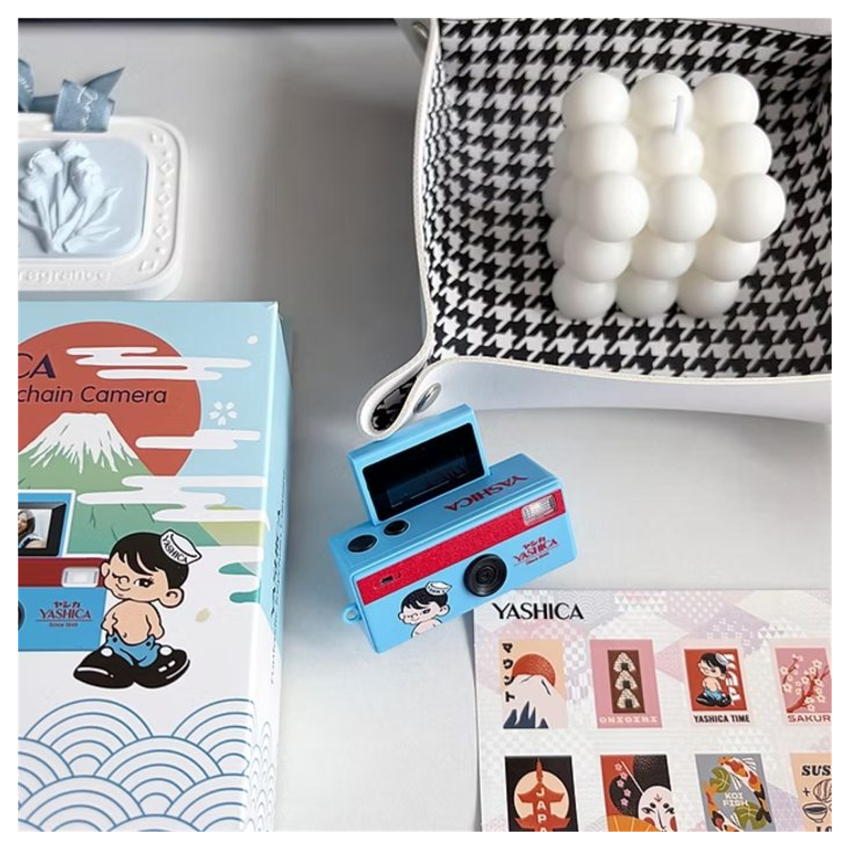 Mini caméra Yashica bleue avec boîte, planche d'autocollants, plateau blanc et bougie.