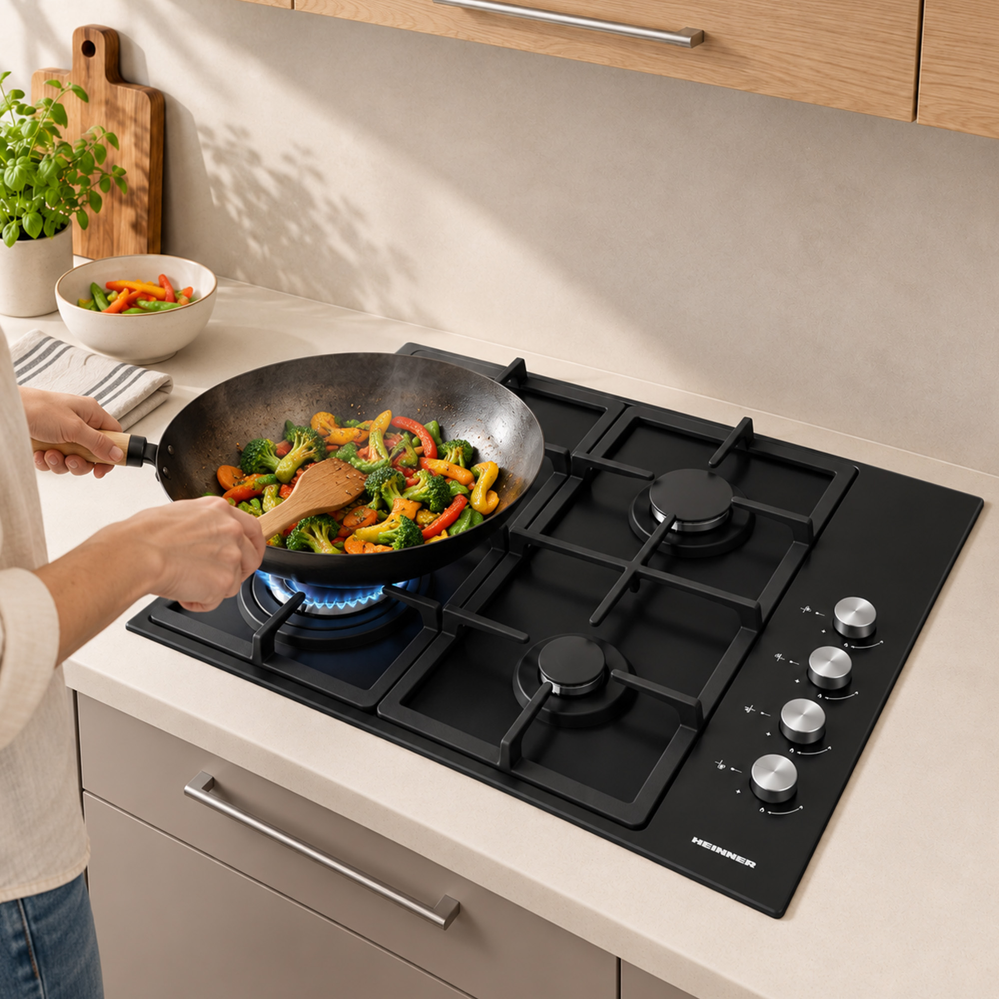 A person stirs vegetables in a pan on a black gas stovetop in a modern kitchen.