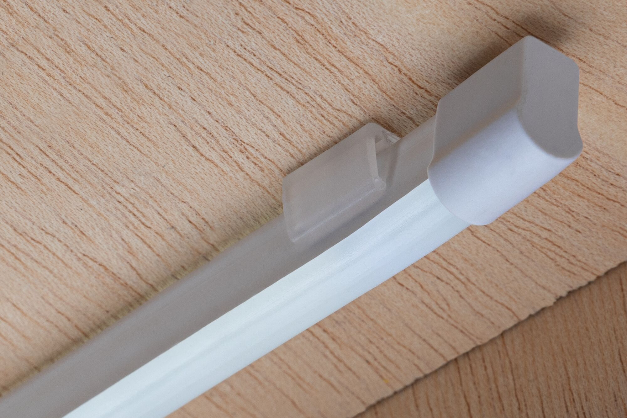 Eine weiße LED-Profilleiste mit Endkappe ist an einer hellbraunen Holzoberfläche befestigt.