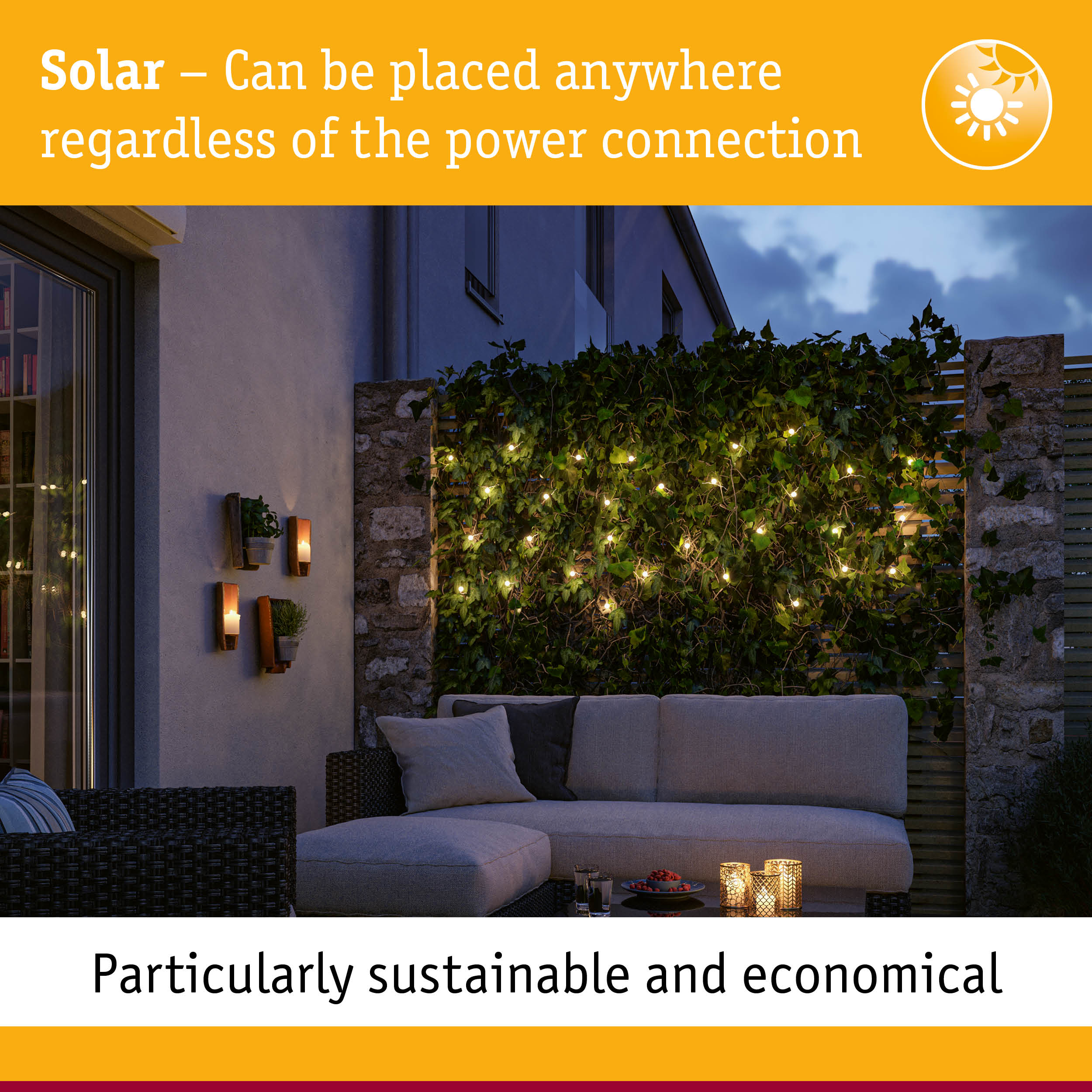 Eine Terrasse in der Dämmerung mit Sofa, Lichterkette an einer grünen Wand und Kerzen.