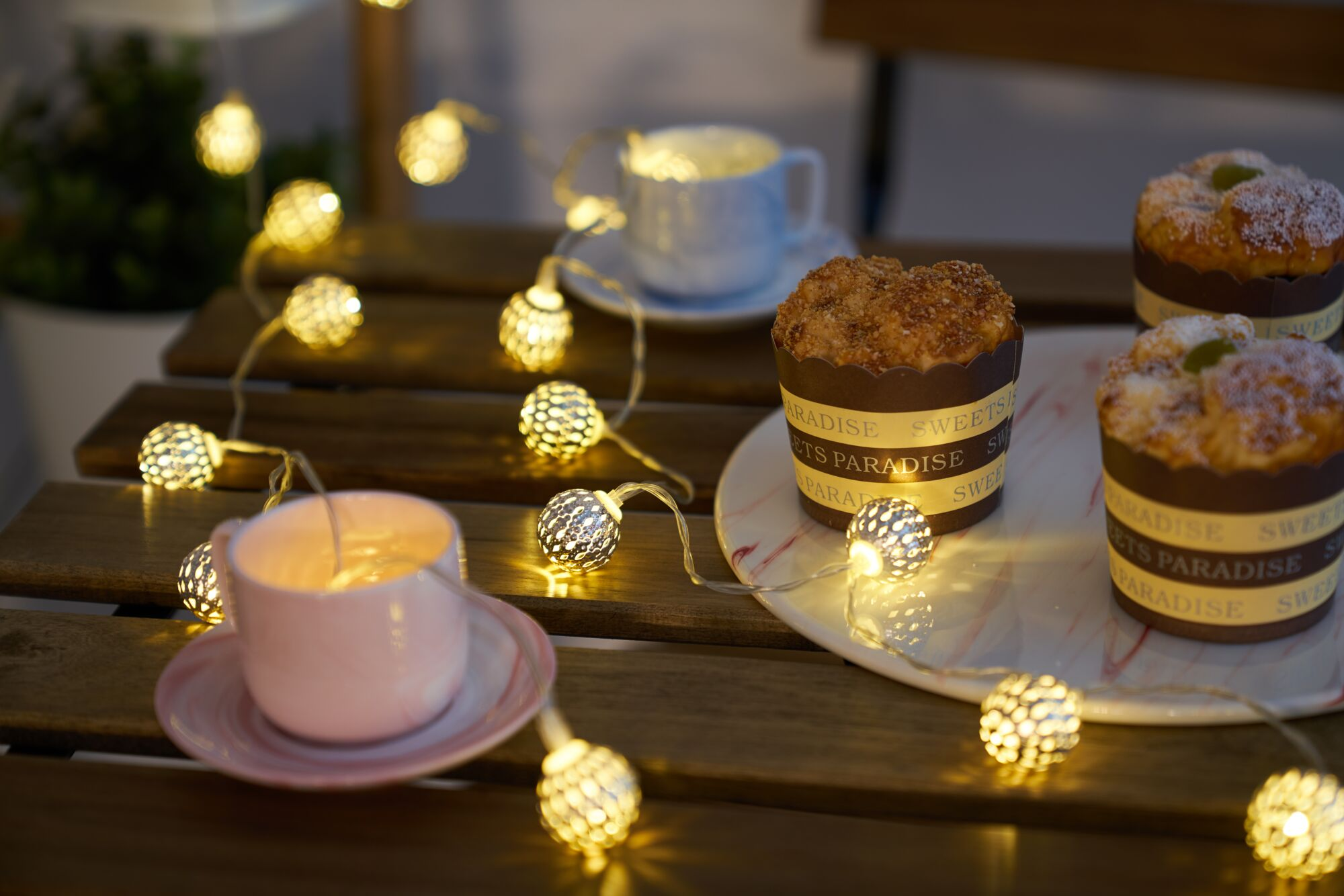 Muffins und Tassen auf Holztisch, beleuchtet mit Lichterkette.