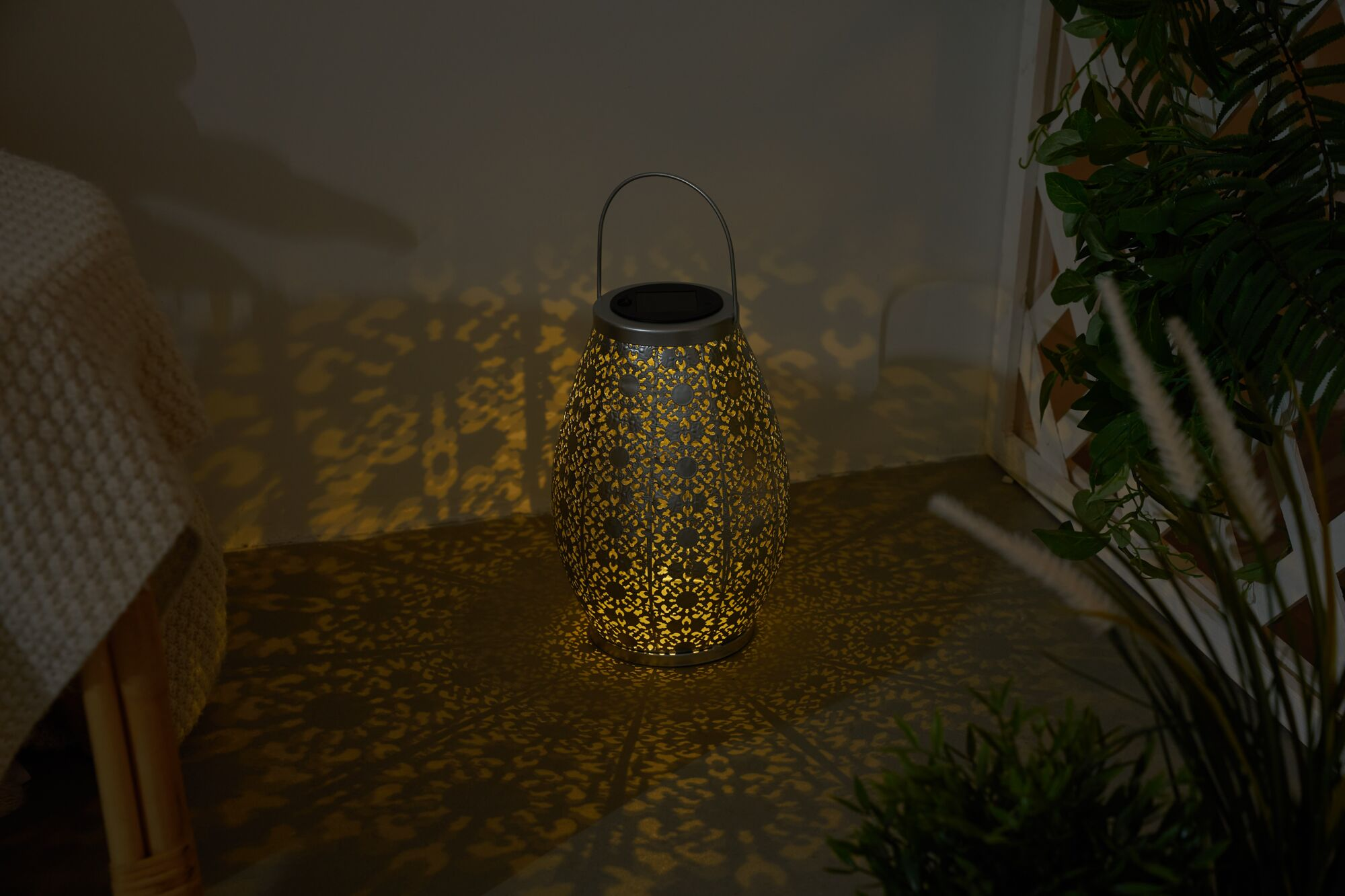 Eine dekorative Metalllaterne mit Mustern, die warmes Licht und filigrane Schatten an Wand und Boden wirft.