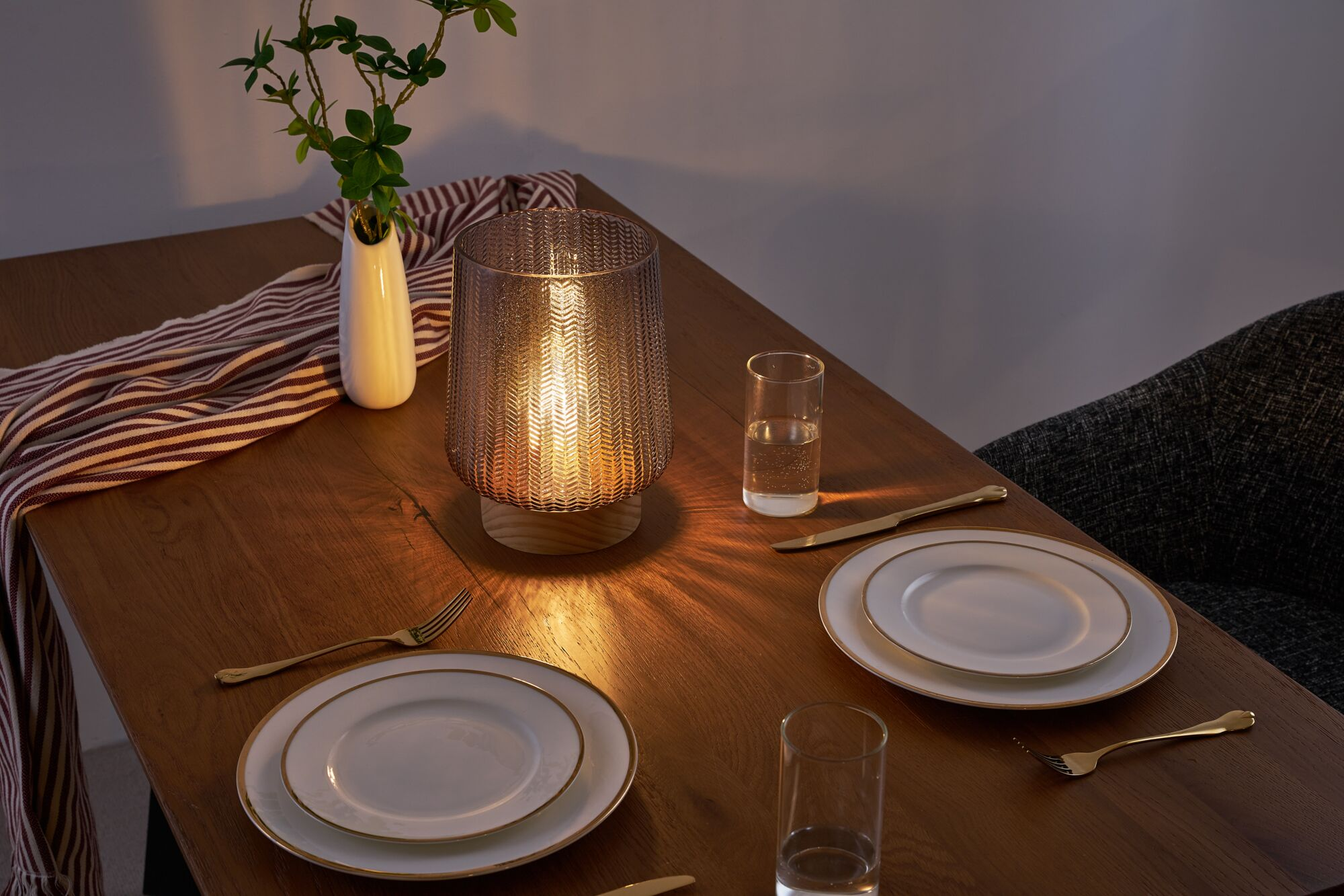 Beleuchtete Tischlampe auf Holztisch mit Tellern, Gläsern und einer Vase.