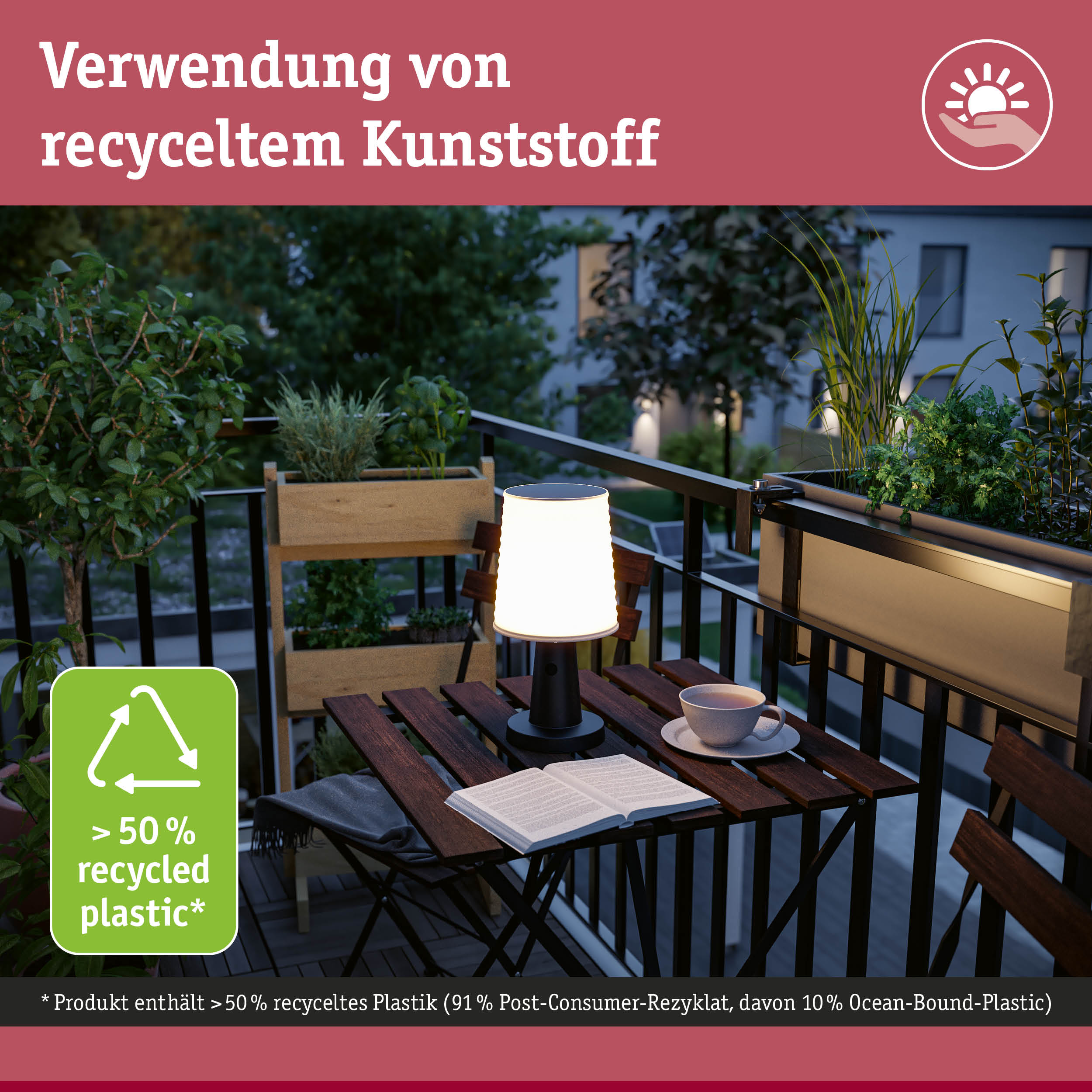 Beleuchteter Holztisch auf einem Balkon bei Dämmerung mit Lampe, Buch und Tasse.