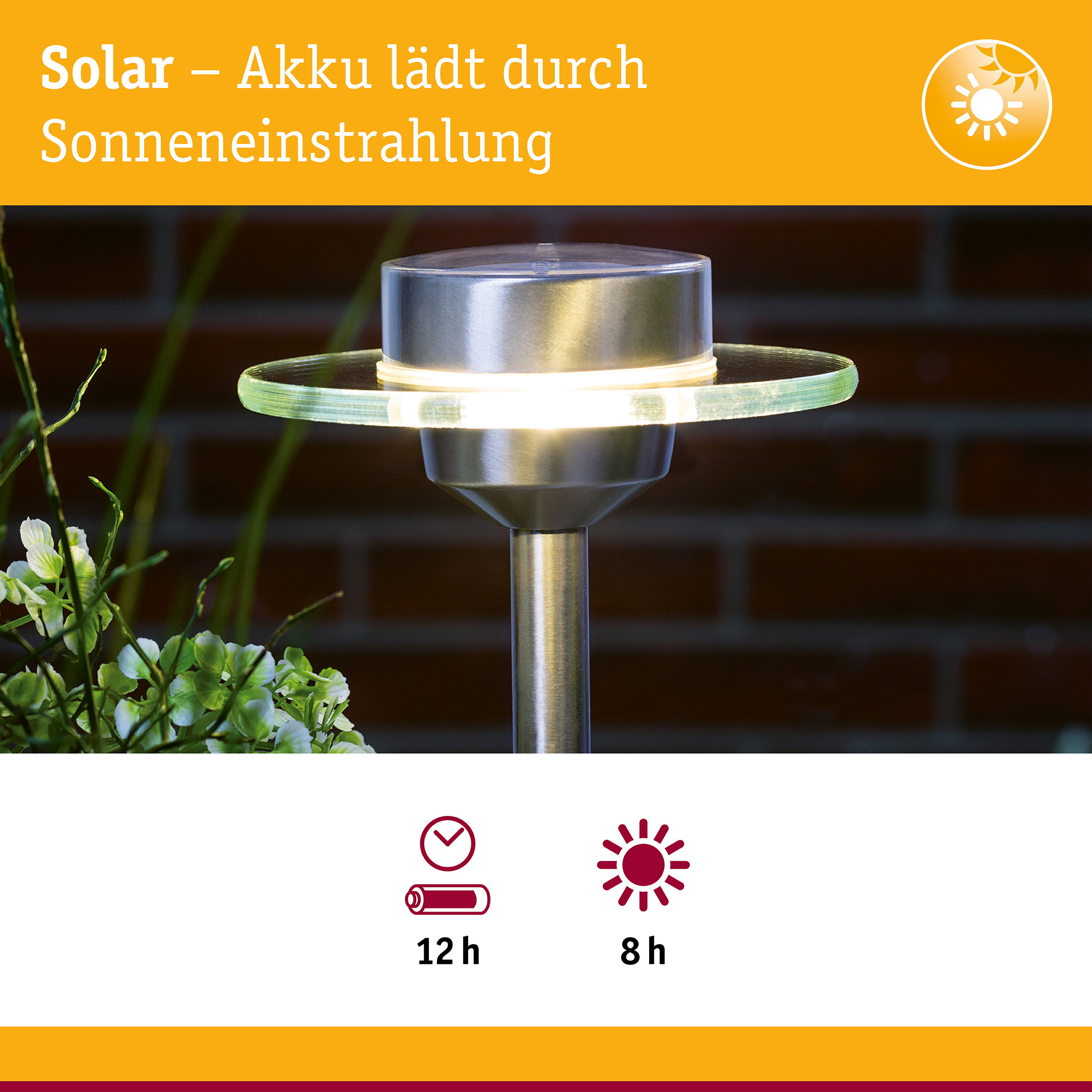 Solar-Wegeleuchte aus Edelstahl mit leuchtender Glasscheibe, im Hintergrund eine Ziegelwand und Pflanzen.