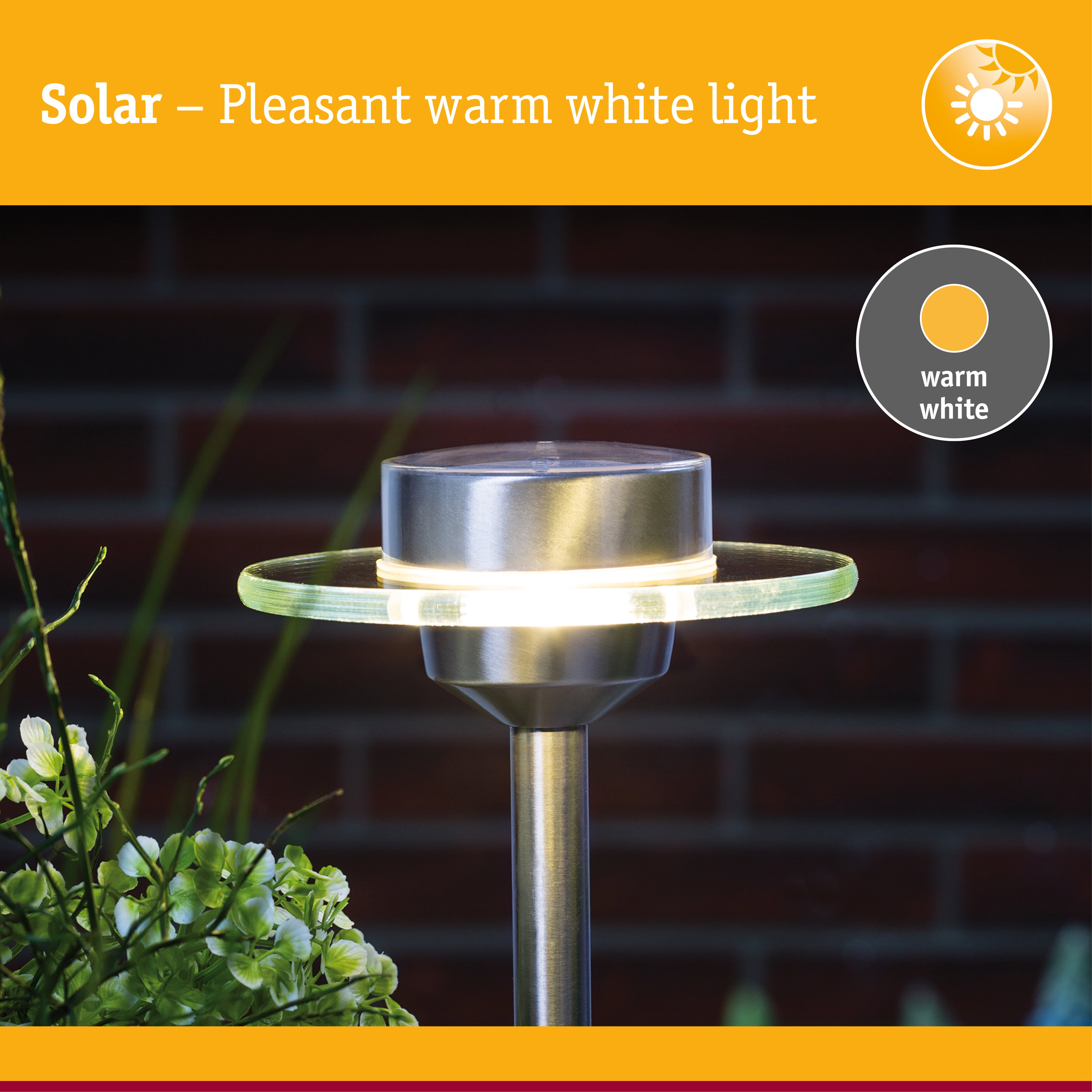 Eine solarbetriebene Gartenleuchte leuchtet warmweiß vor einer dunklen Ziegelwand.