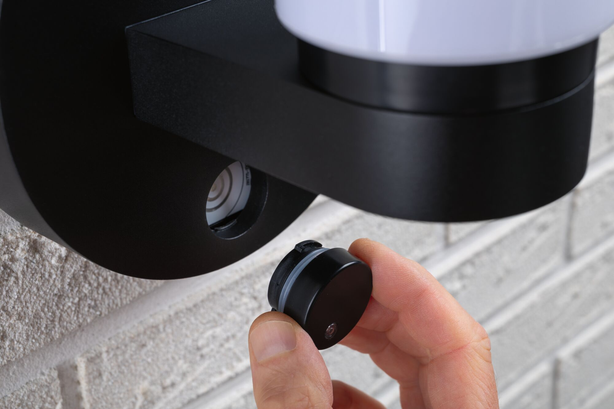 Eine Hand setzt einen kleinen runden Deckel in eine schwarze Wandlampe ein.