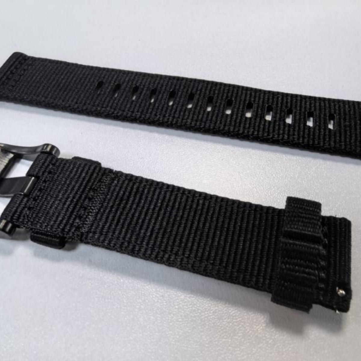 Un cinturino per orologio in nylon nero con fibbia e fori su sfondo bianco.