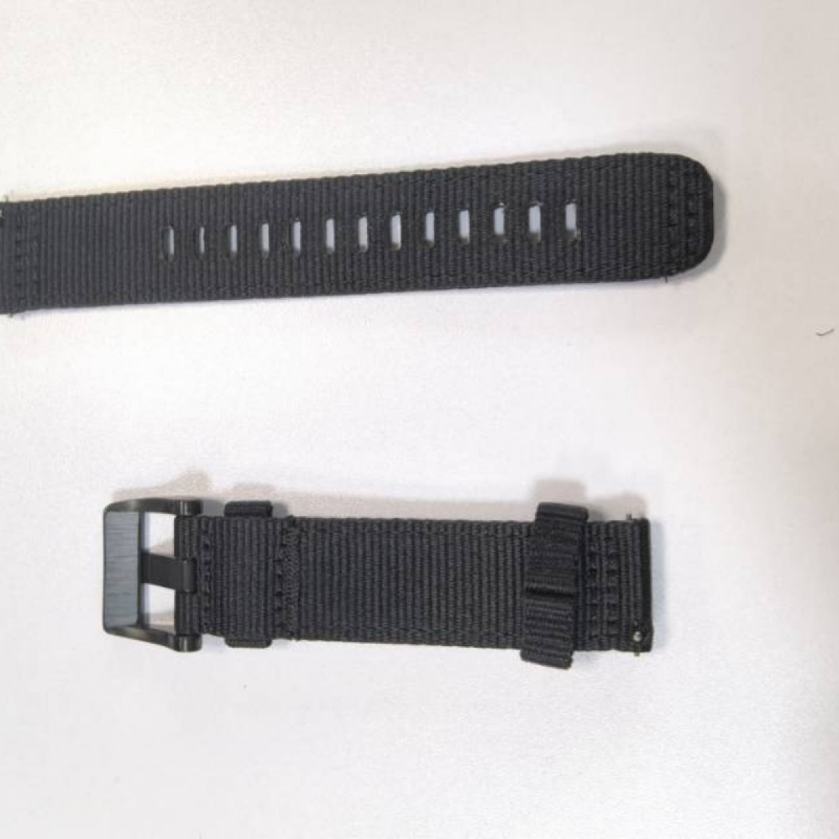 Due pezzi di cinturino per orologio in tessuto nero con fibbia nera su fondo grigio.