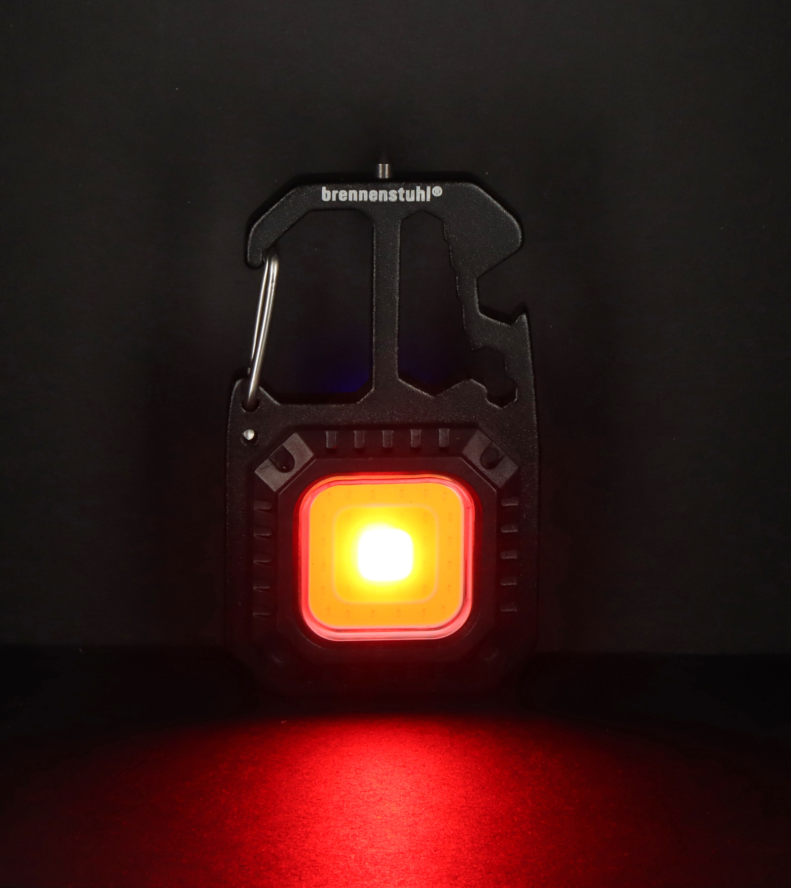 Schwarzes tragbares LED-Arbeitslicht mit roter Beleuchtung vor dunklem Hintergrund.