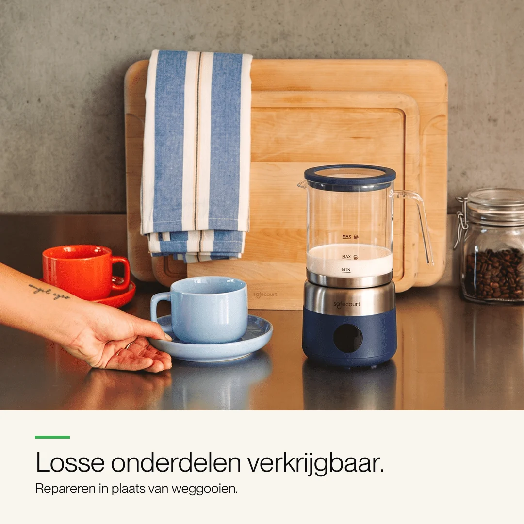 Milk frother on a counter with blue and red cups, wooden cutting board, and coffee beans jar in the background.