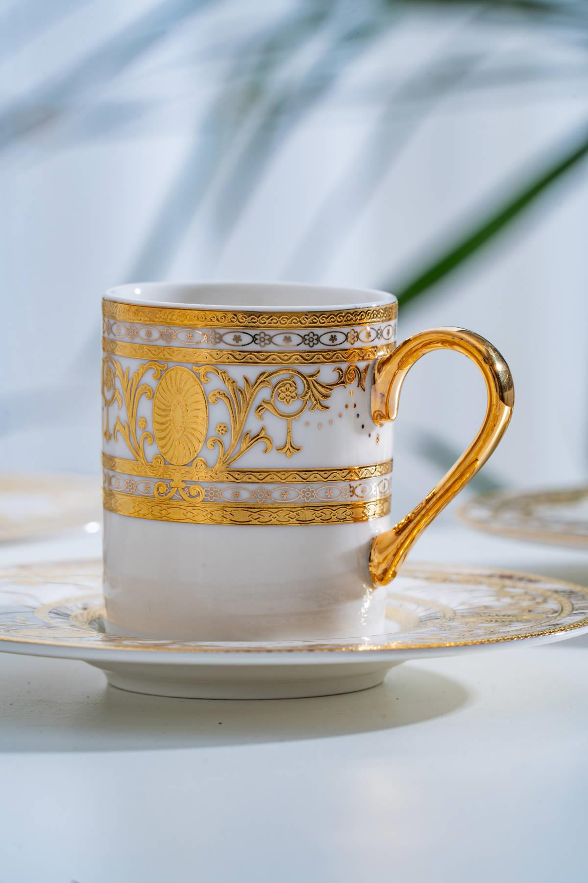 Karmaşık altın desenli ve parlak altın kulplu beyaz porselen çay fincanı ve tabağı.