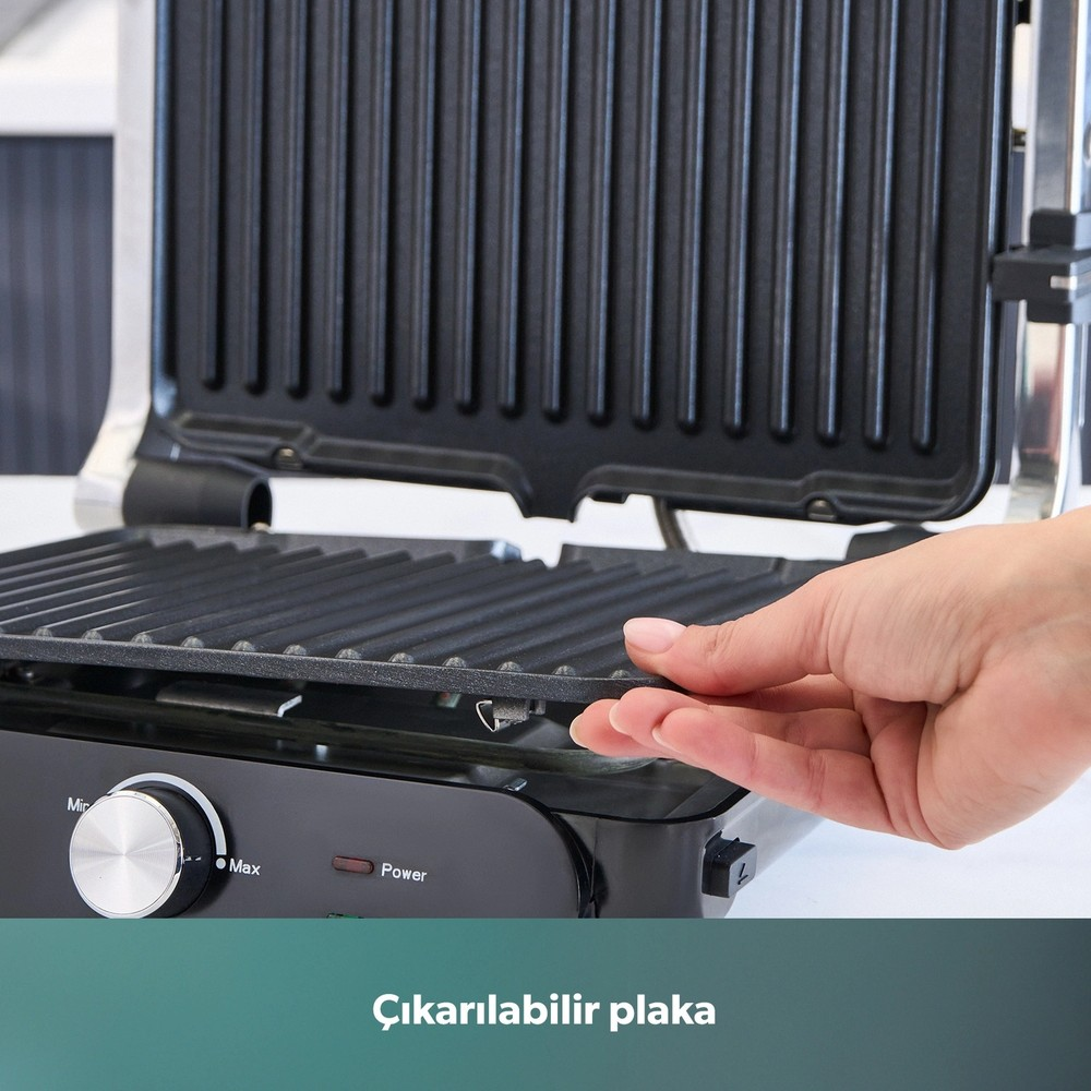Bir el, siyah bir elektrikli ızgaranın çıkarılabilir ızgara plakasını çıkarıyor.