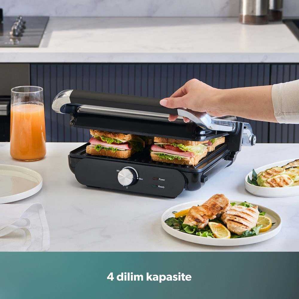 El, sandviçli siyah tost makinesini kapatıyor; tezgahta tabak ve meyve suyu var.