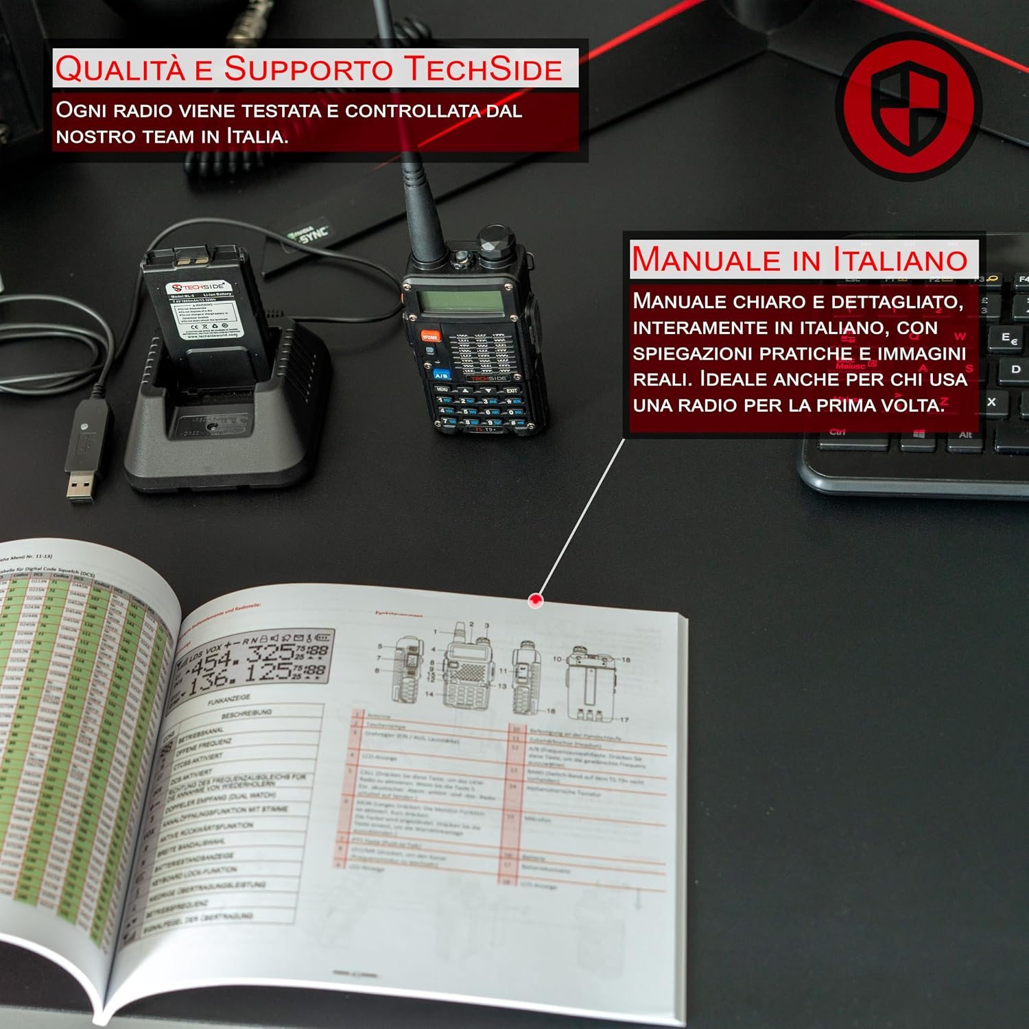 Una radio walkie-talkie nera con base di ricarica e manuale aperto su una scrivania scura accanto a una tastiera.