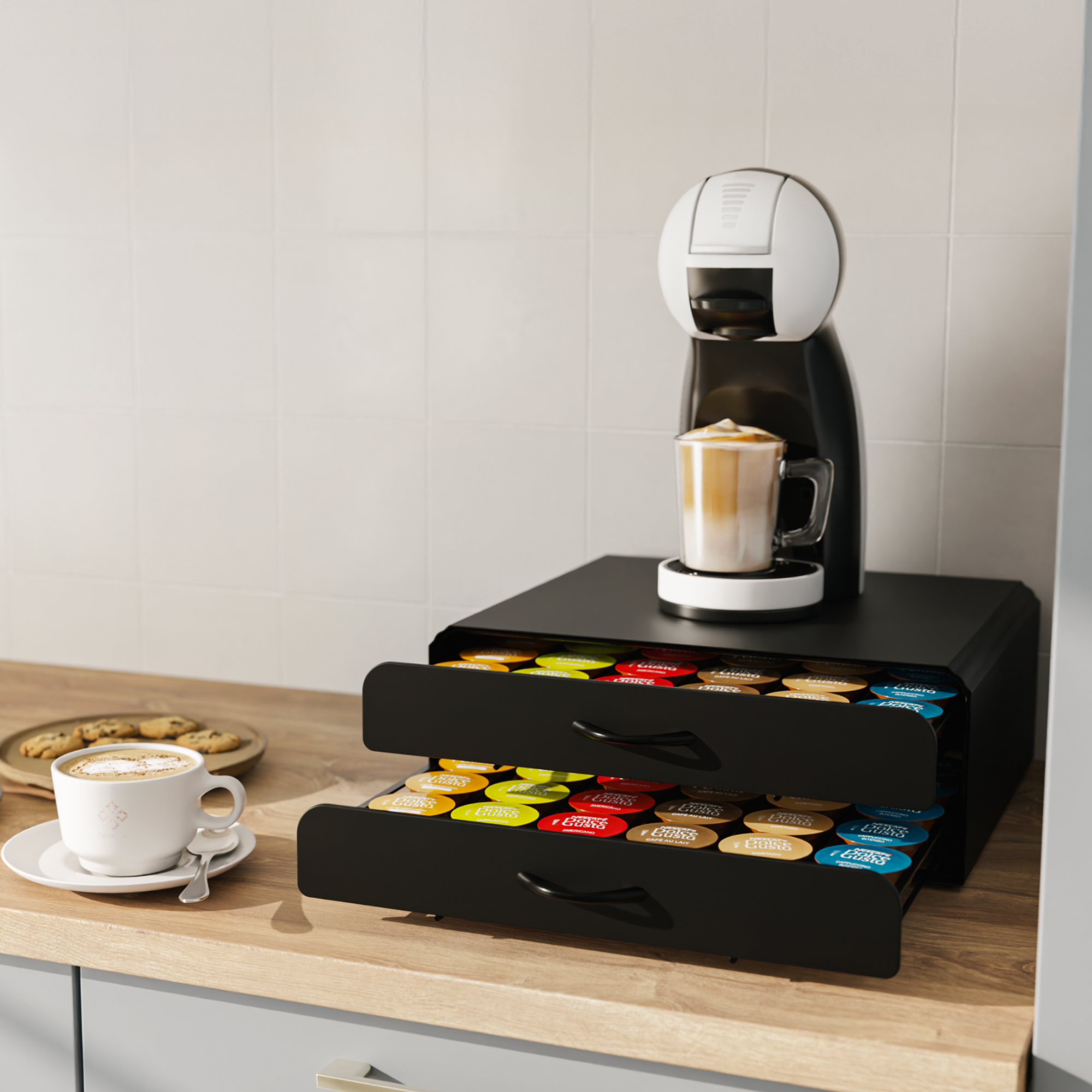 Eine Kaffeemaschine auf einer Schublade mit Kaffeekapseln, daneben eine Tasse Cappuccino und Kekse auf einer Theke.