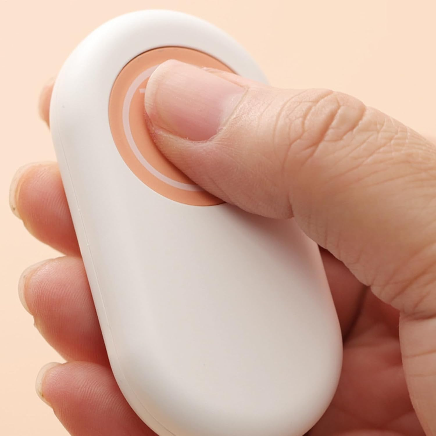 Eine Hand drückt auf den orangefarbenen runden Knopf einer ovalen weißen Fernbedienung vor neutralem Hintergrund.