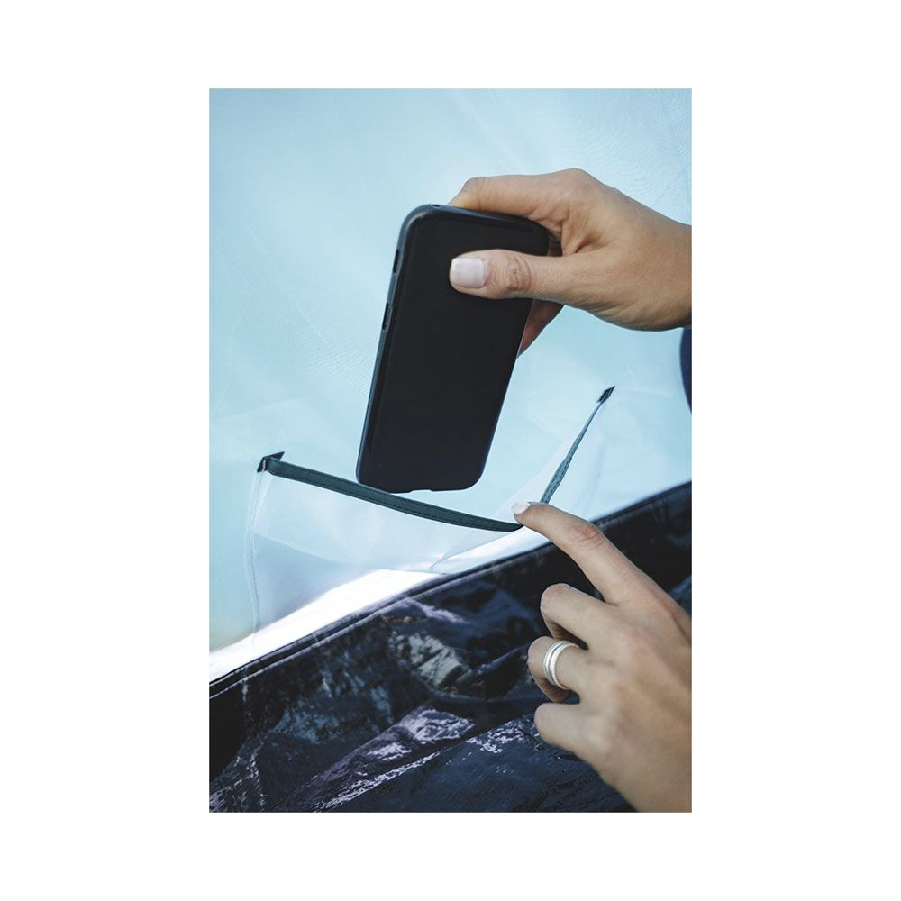 Une main place un smartphone noir dans une petite poche sur la paroi d'une tente.