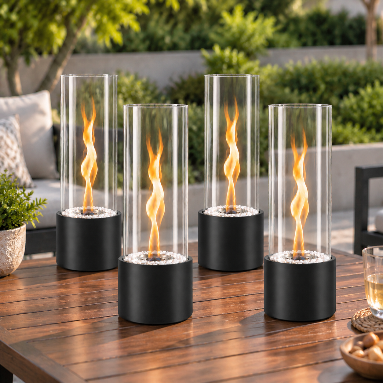 Vier zylindrische Tischkamine mit brennenden Flammen stehen auf einem Holztisch im Garten.
