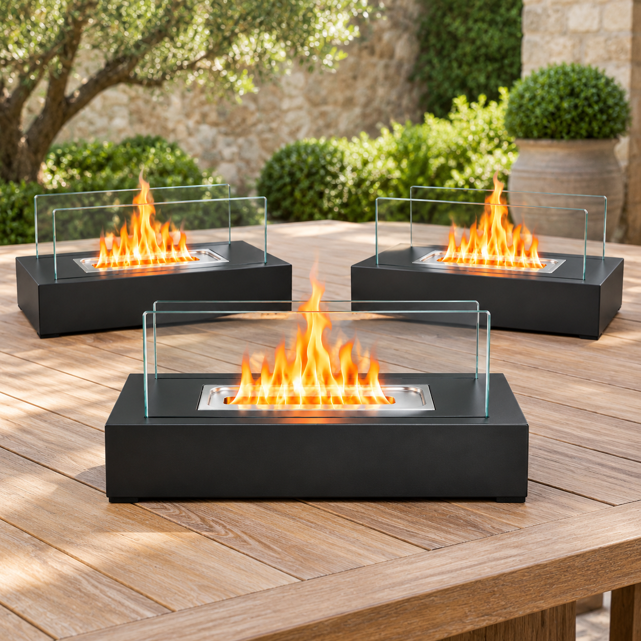 Drei moderne, schwarze Tischkamine mit brennenden Flammen stehen auf einem Holztisch in einem Garten.