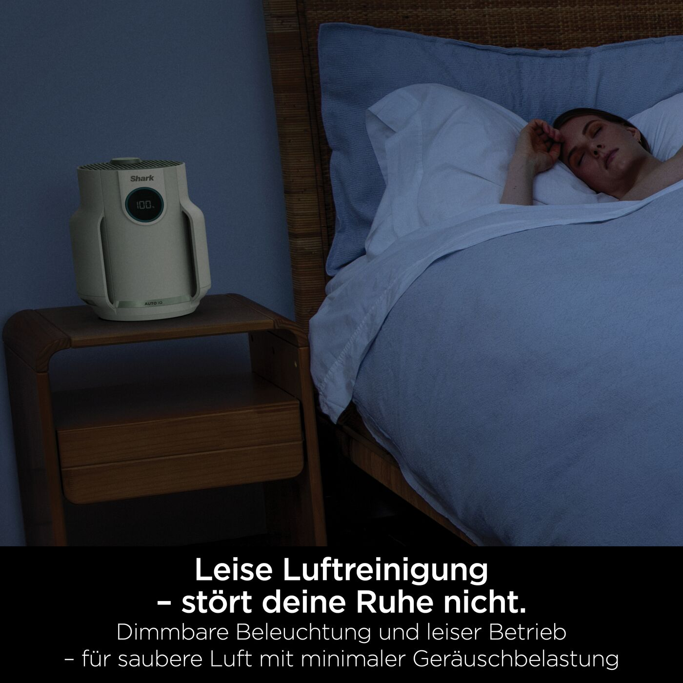 Ein Shark-Luftreiniger steht auf einem Nachttisch neben einem Bett, in dem eine Frau schläft.