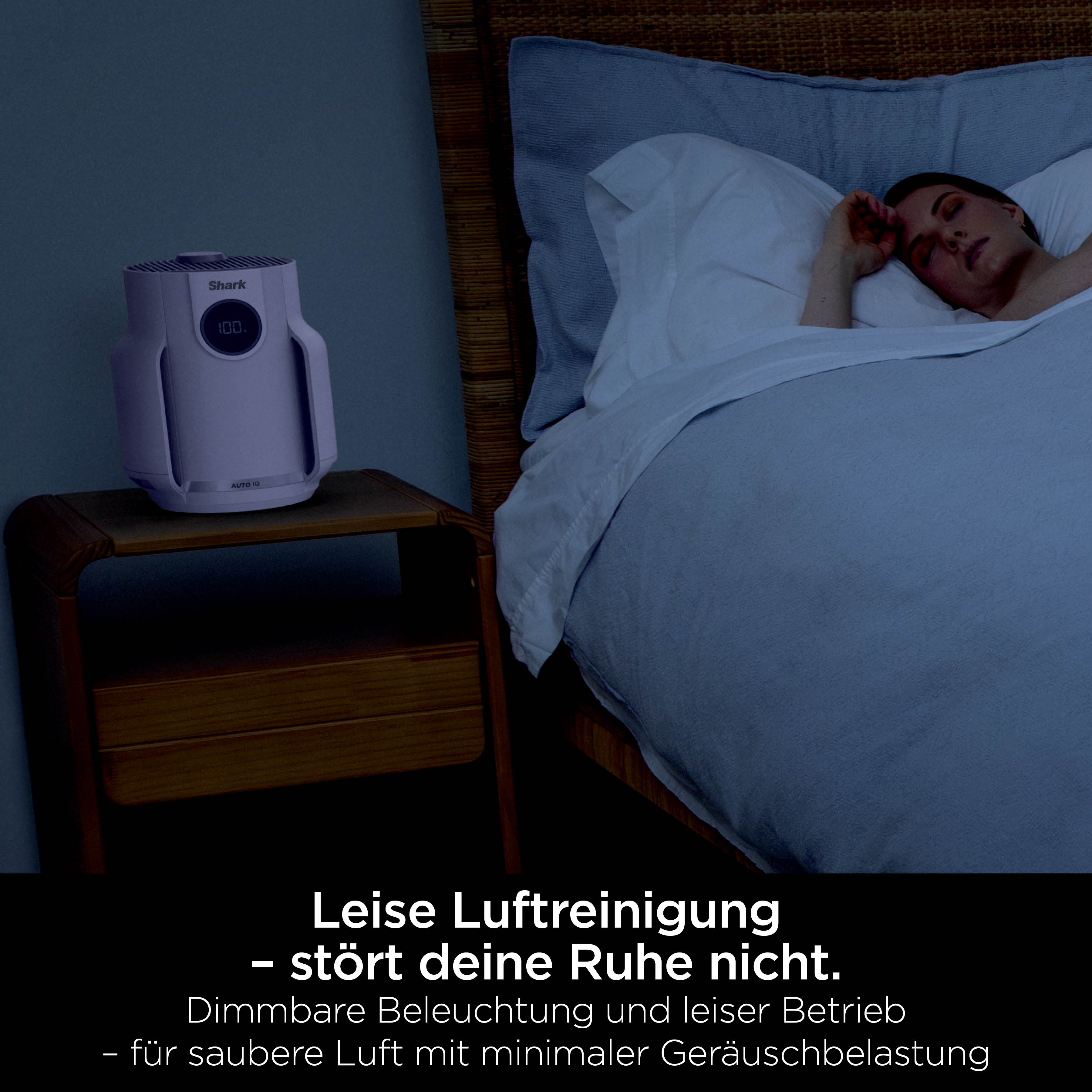 Ein weißer Shark Luftreiniger auf einem Nachttisch im Schlafzimmer, während jemand schläft.