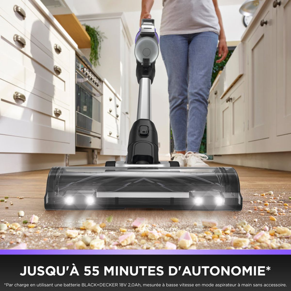 Una aspiradora con luces limpia restos de comida en un suelo de madera en una cocina.
