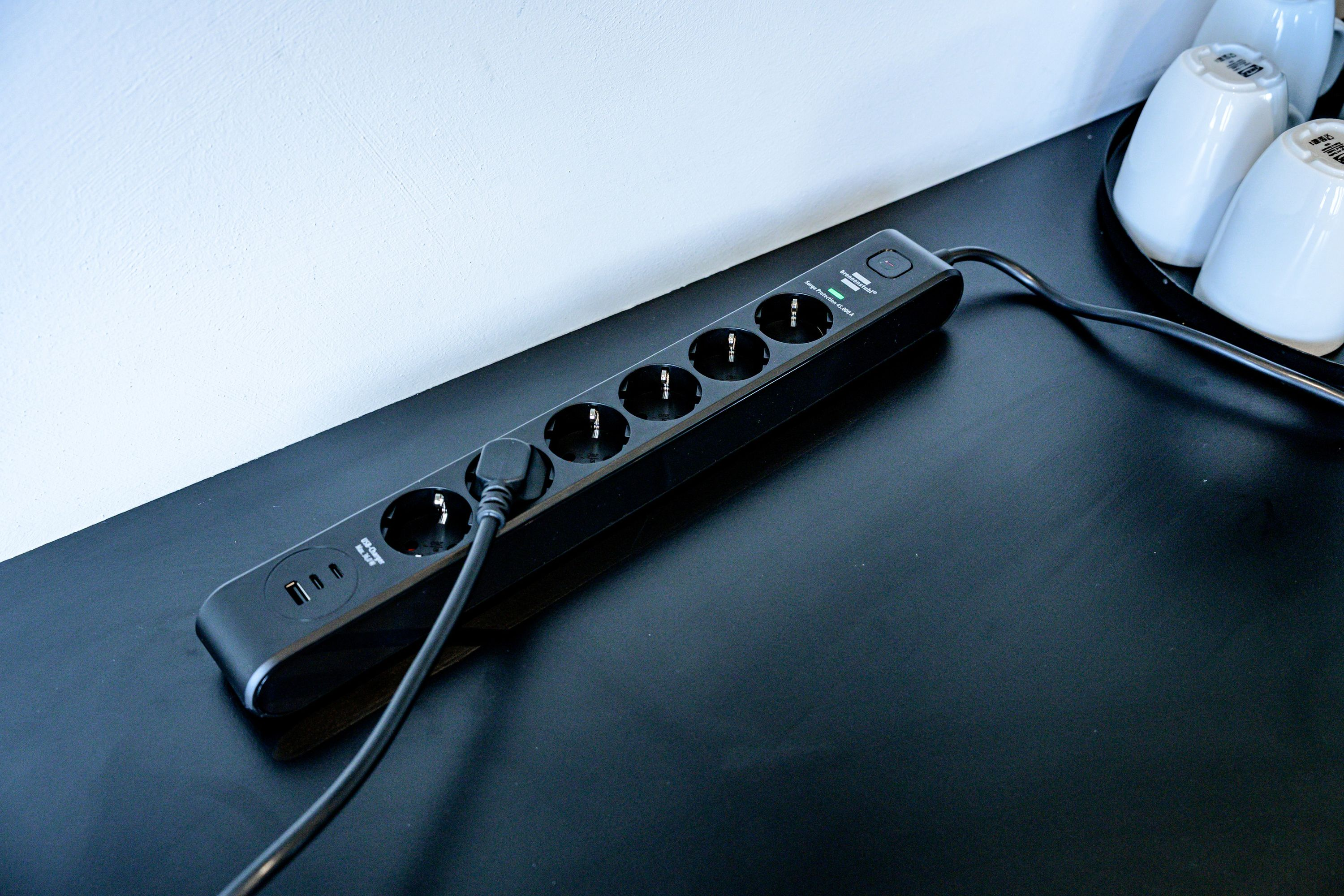 Eine schwarze Mehrfachsteckdose mit USB-Anschlüssen liegt auf einem dunklen Tisch, ein Stecker ist eingesteckt.